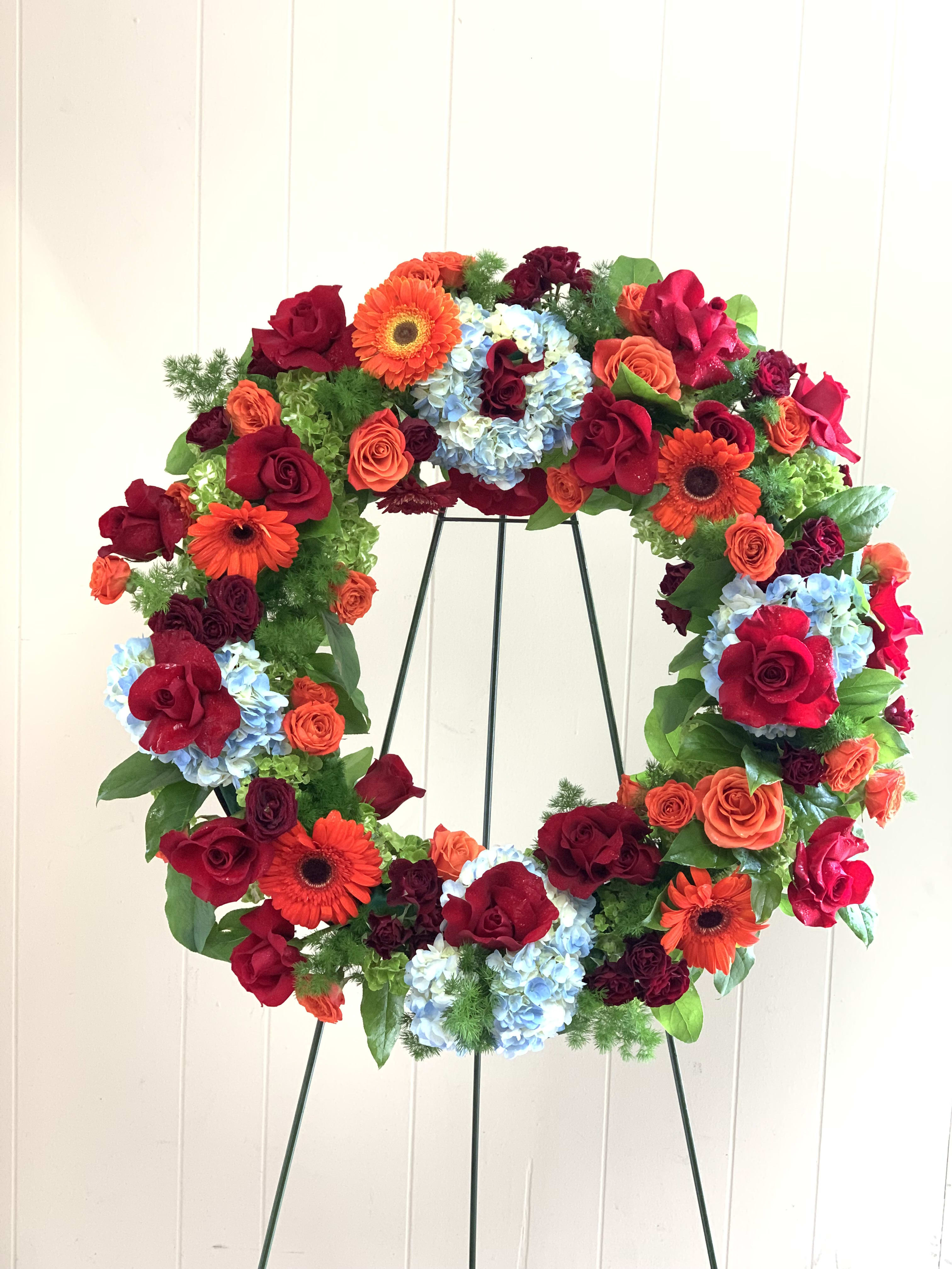 SYM11 - Colorful Funeral Wreath - Like a beacon of love and hope, this glorious funeral wreath of colorful hydrangea, roses and gerber daisies echoes the joy of your precious memories.Delivered on a wire easel.