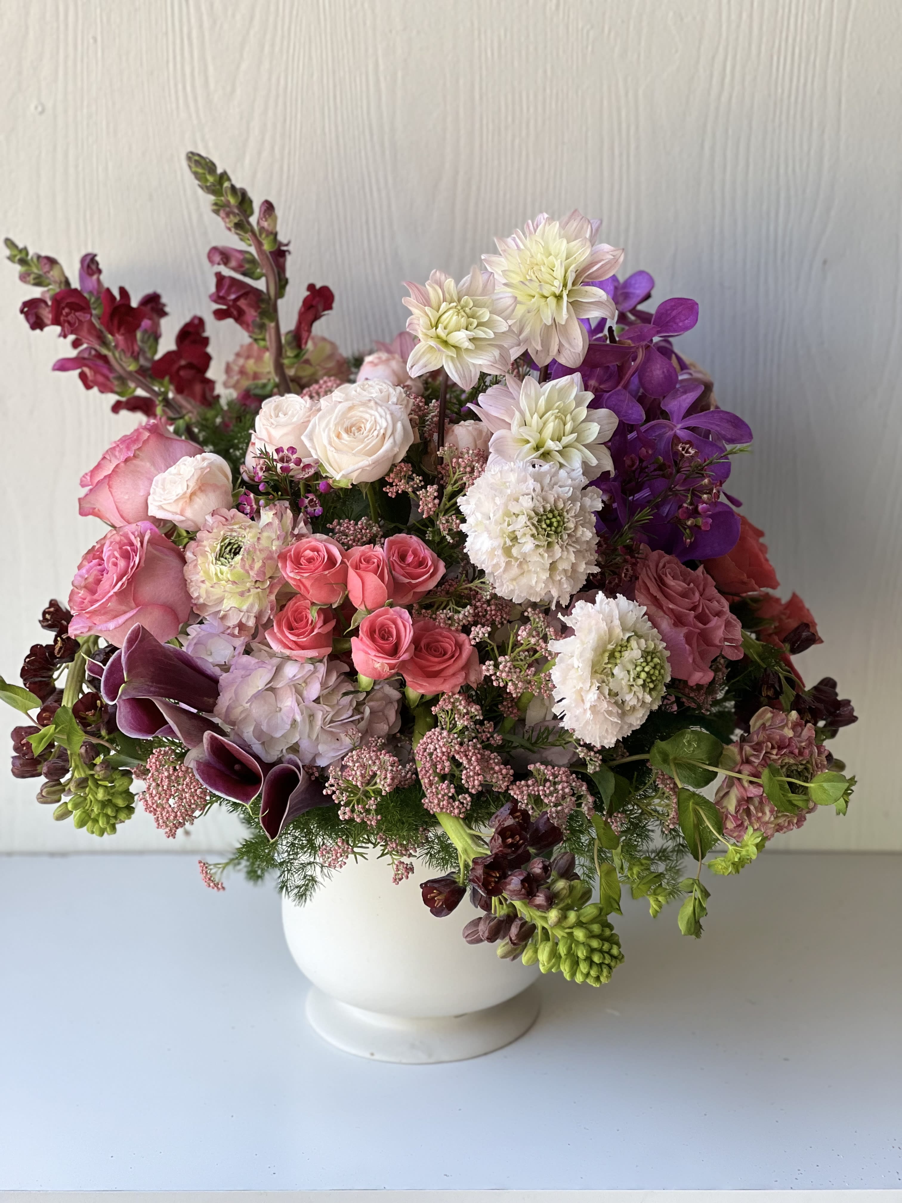 Mixed pink, white, and purple flowers arranged in a white vase