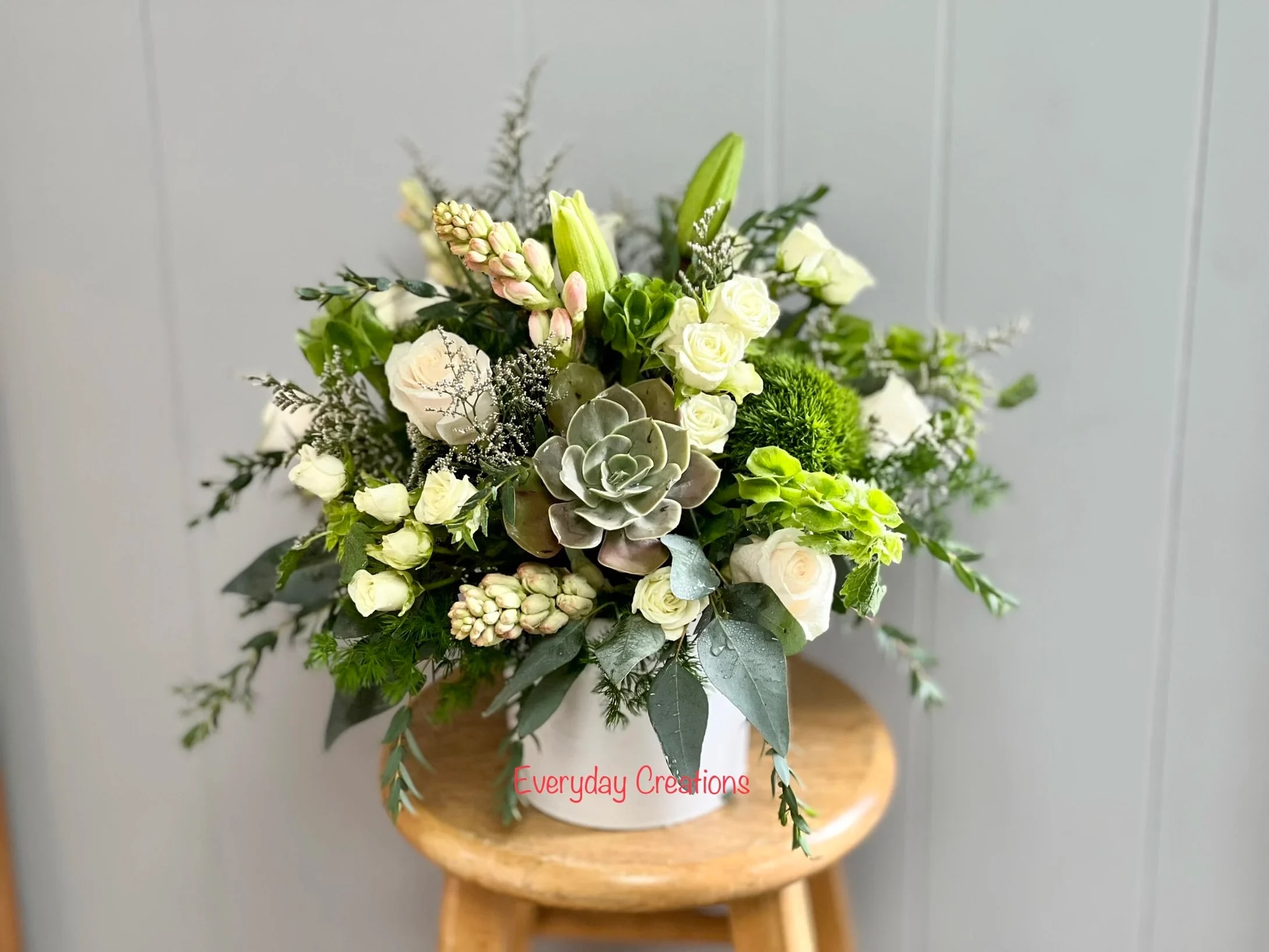White and green floral arrangement in a white container with a succulent center