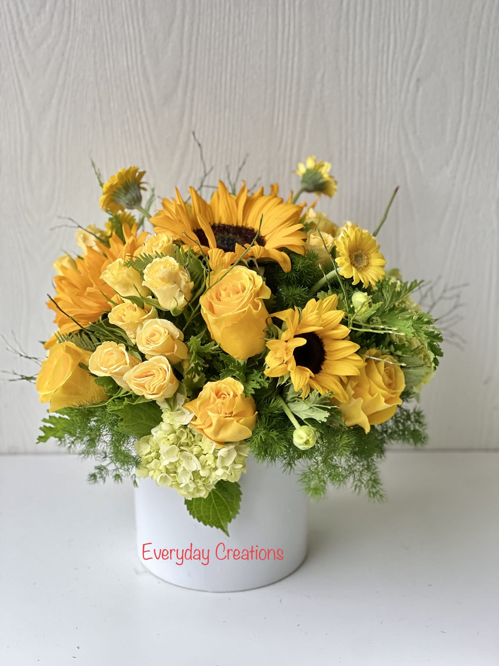 Yellow roses and sunflowers arranged in a white vase