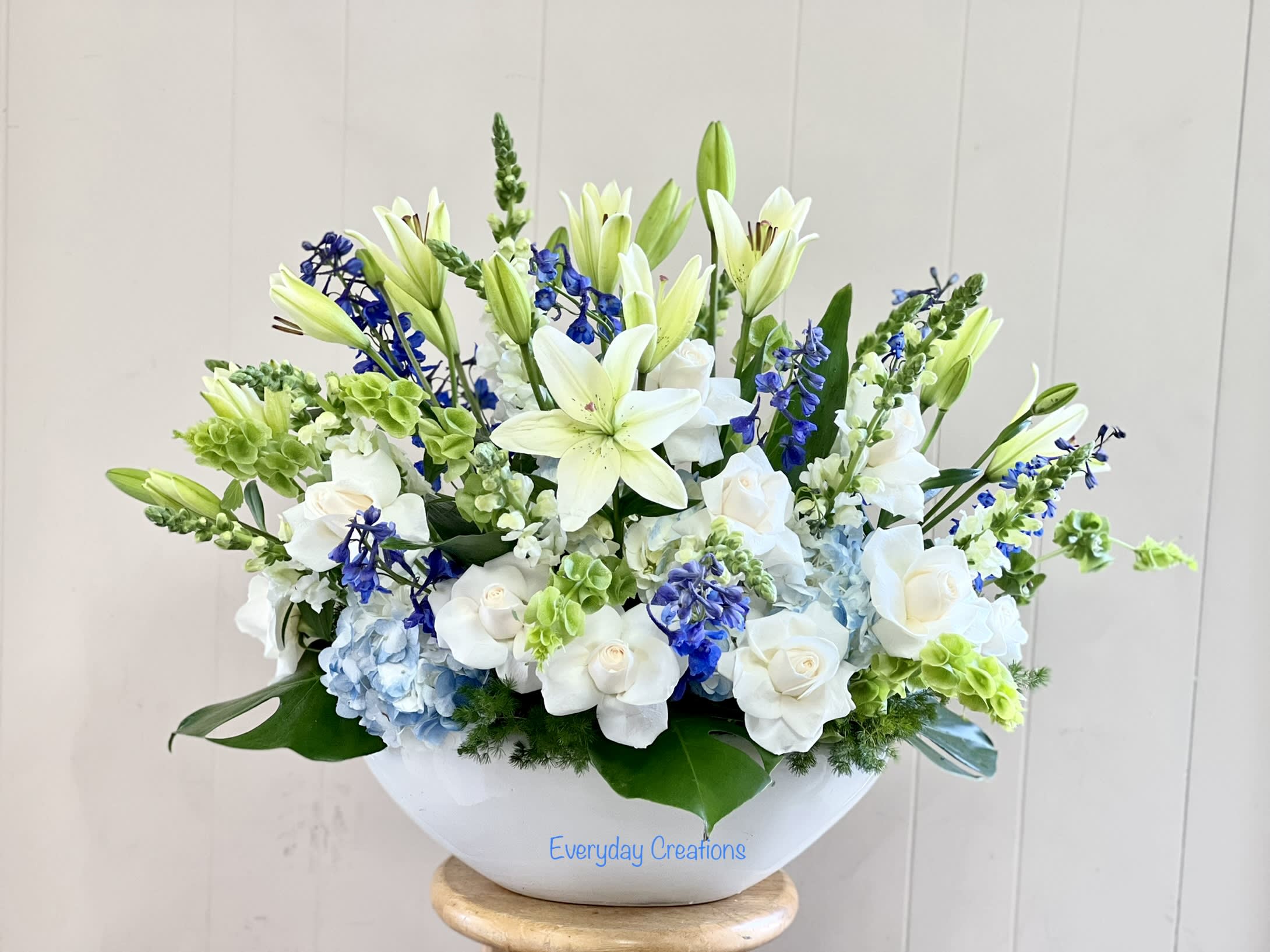 White lilies and roses arranged in a white bowl with blue accents