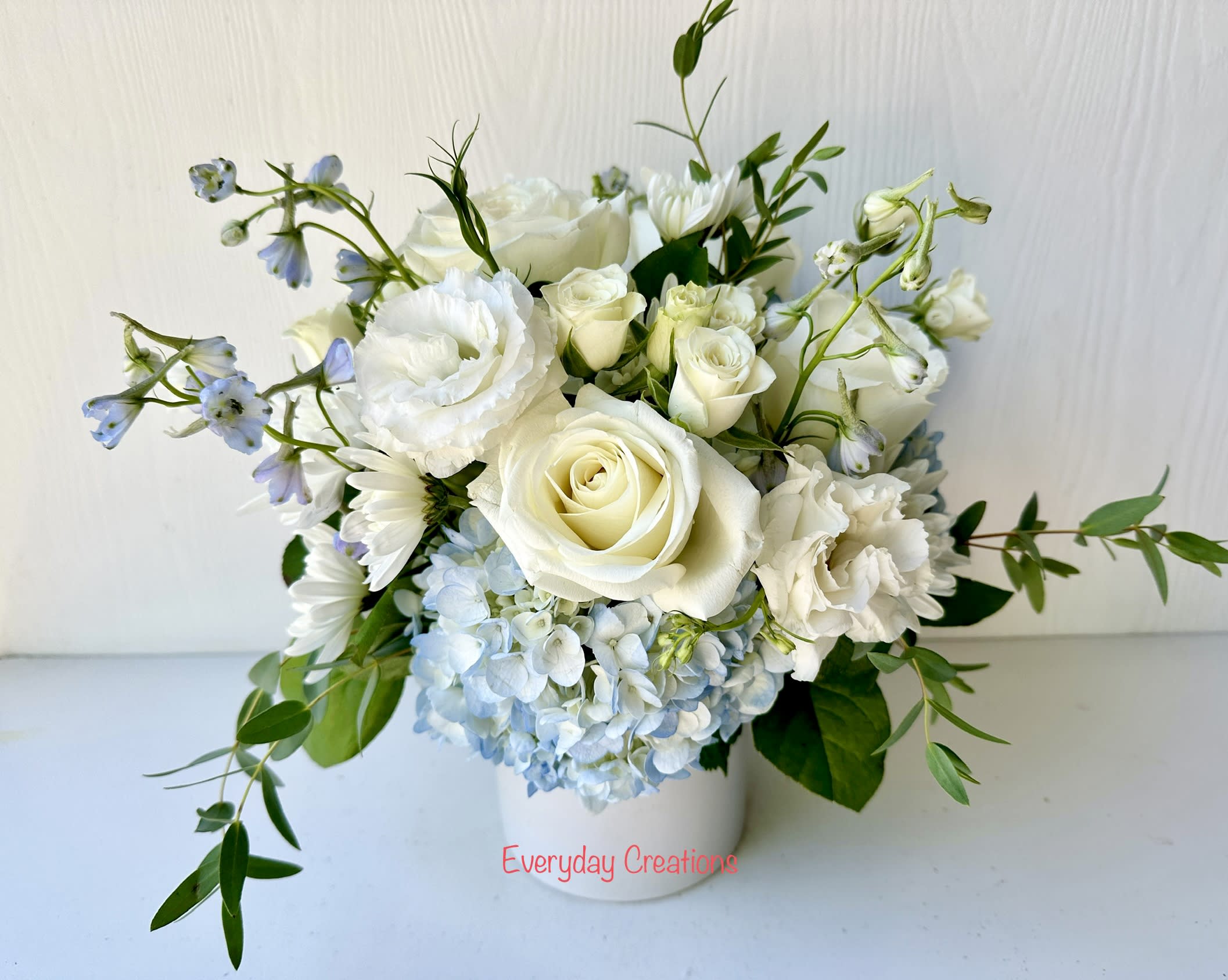 White roses and pale blue hydrangeas in a white vase