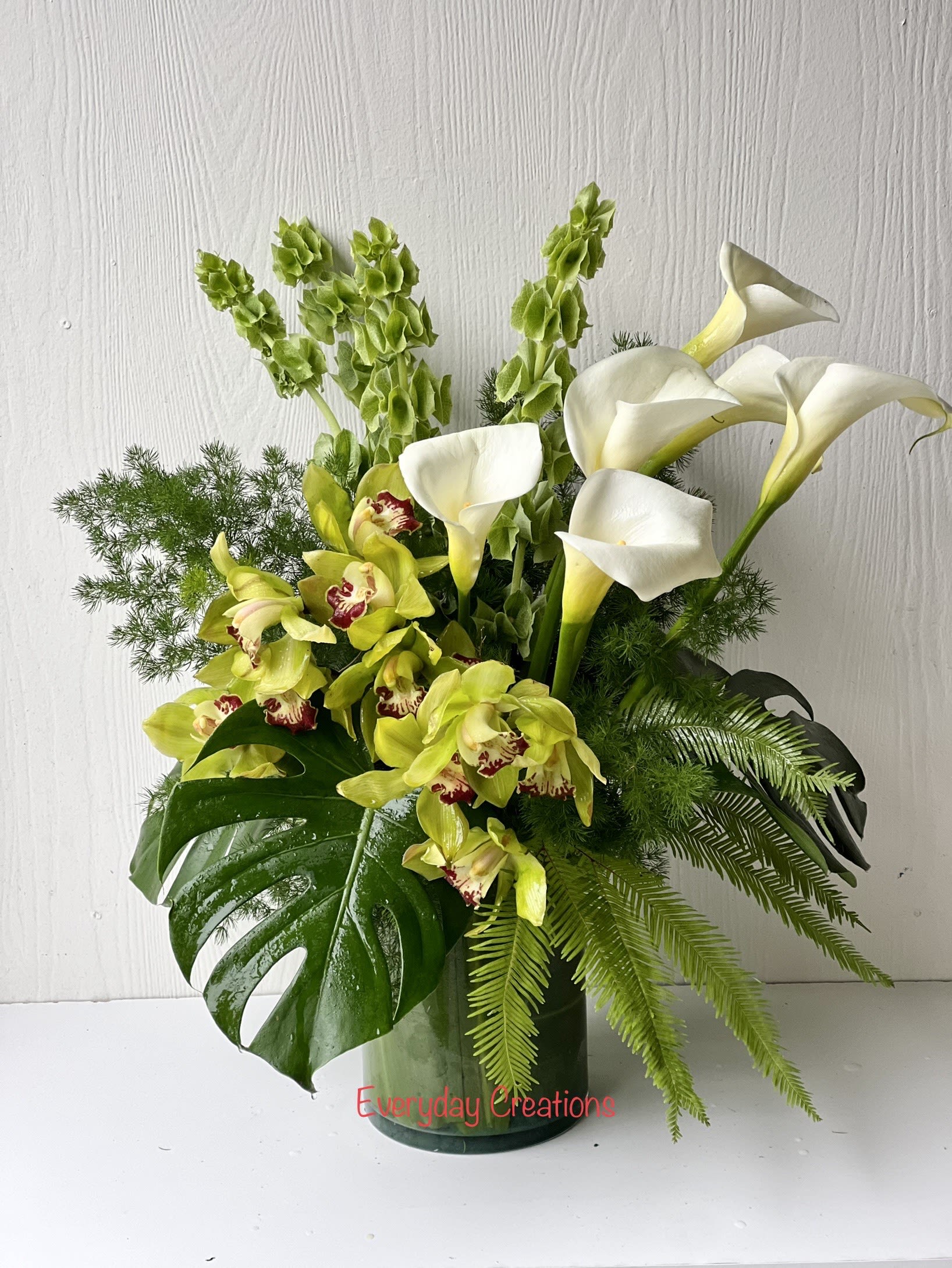White calla lilies and green orchids in a glass vase