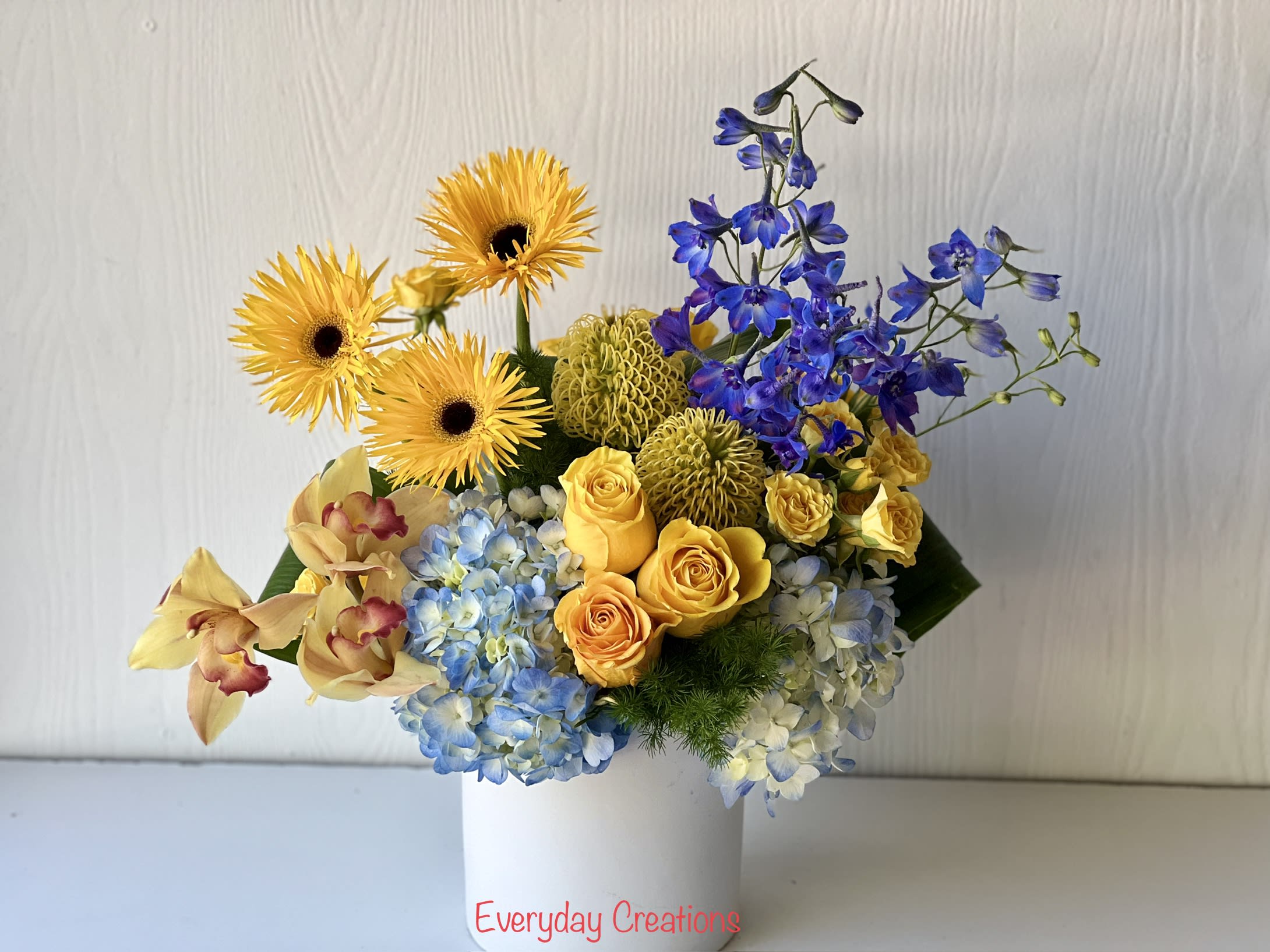 Bouquet of yellow gerbera daisies, blue hydrangeas, and yellow roses in a white vase