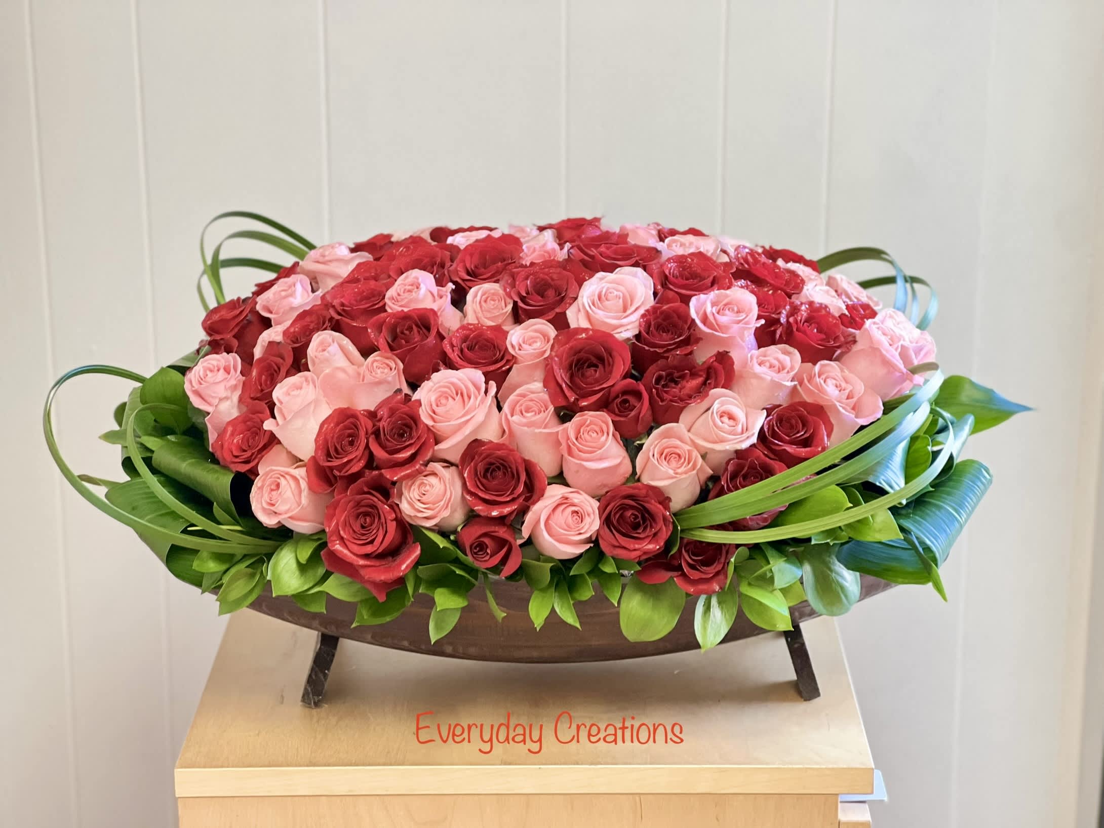 Oval arrangement of red and pink roses in a low wooden container