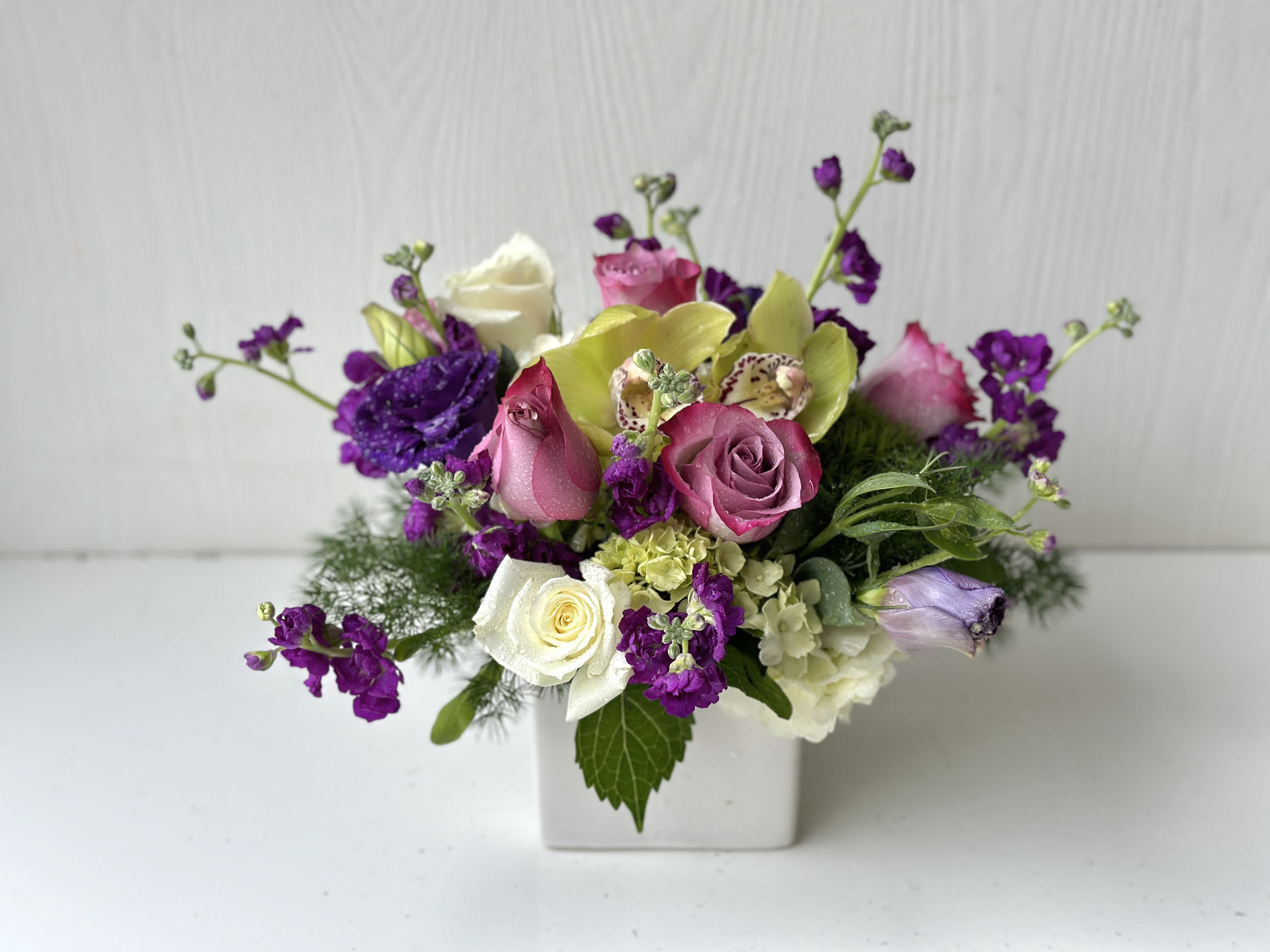 Mixed bouquet of roses, orchids, and purple blooms in a white vase