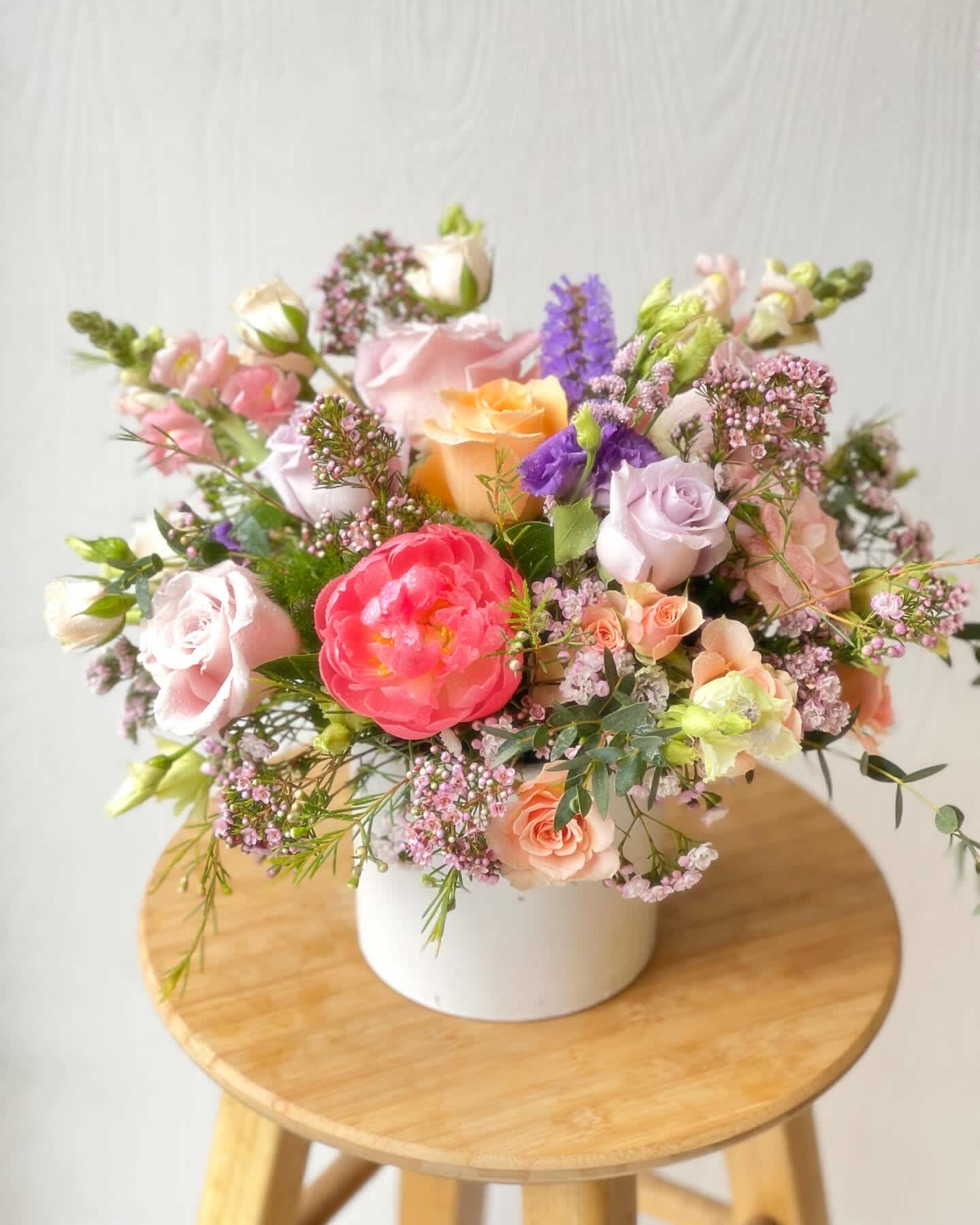 Mixed pastel flower arrangement in a white vase on a wooden stool