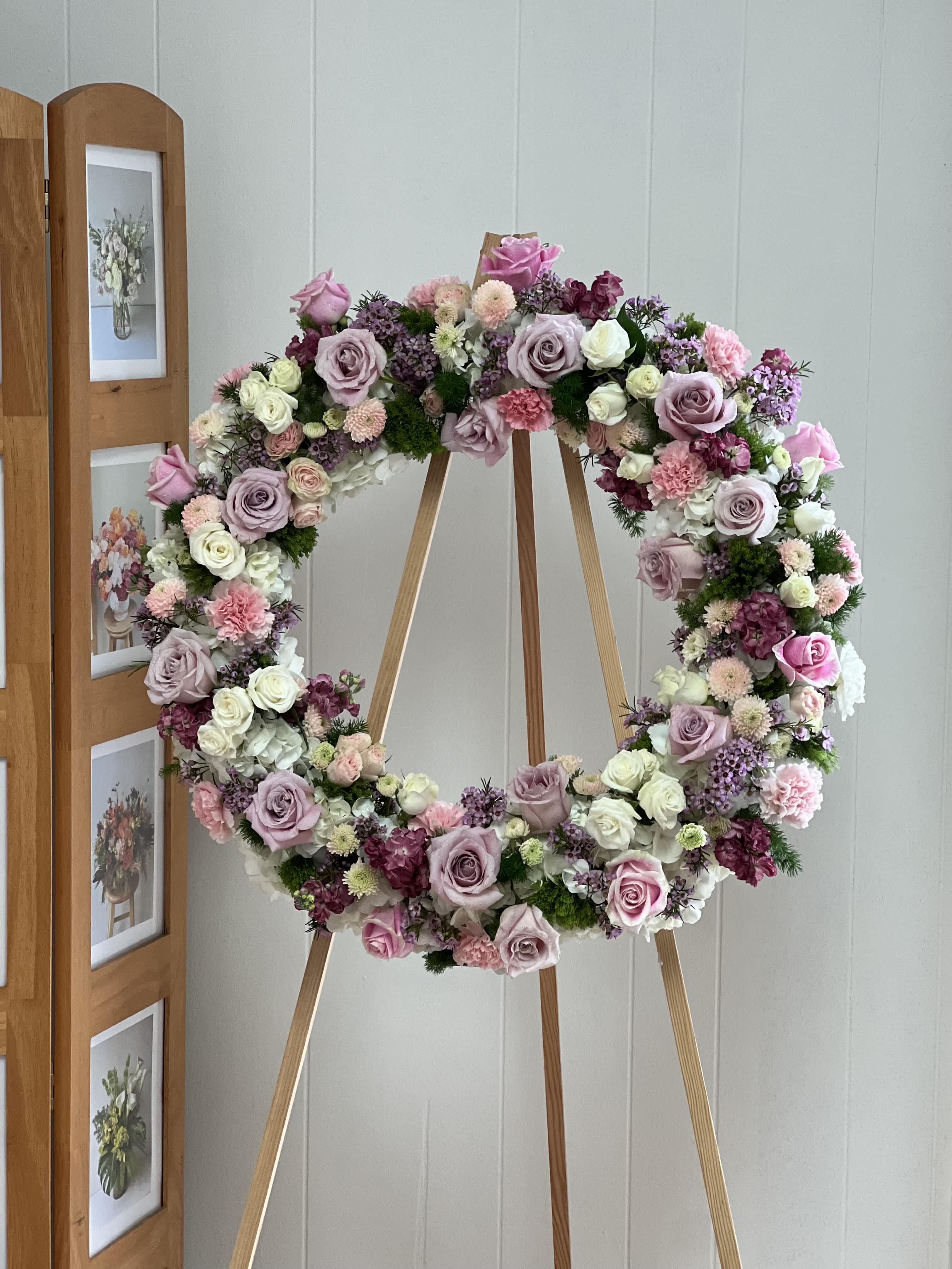 SYM21 - Pink Wreath - The Pink Wreath is a gorgeous and soft standing spray arrangement delivered on a sturdy easel. This feminine style wreath exudes a delicate and ethereal feelings through the use of a beautiful design of daisies and roses, adorned with an airy silky ribbon. The Pink Wreath is a 22" wreath and is an ideal choice for expressing sympathy at a funeral or memorial service or commemorating a special event. 