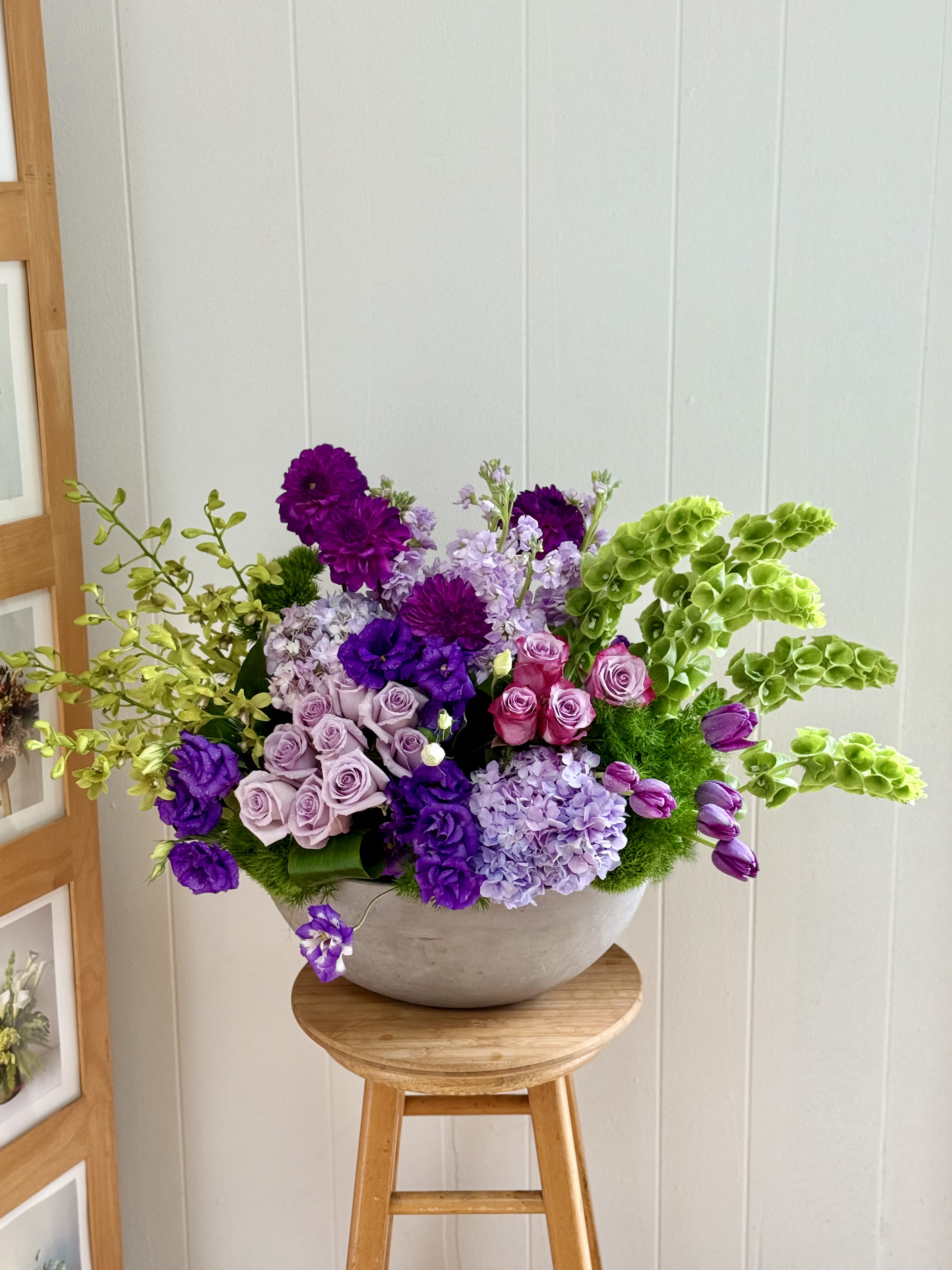 EC90 - Lavender Voyage - This stunning flower arrangement is designed to be long and elegant, making it perfect for an entry table or mantelpiece. It features a beautiful combination of white tulips, lavender roses, blue delphinium, green orchids and white lisianthu in a white ceramic vase. The white tulips add a touch of elegance, while the lavender roses bring a sense of calm and tranquility. This arrangement is sure to impress anyone who sees it and will bring a touch of natural beauty to any room. 