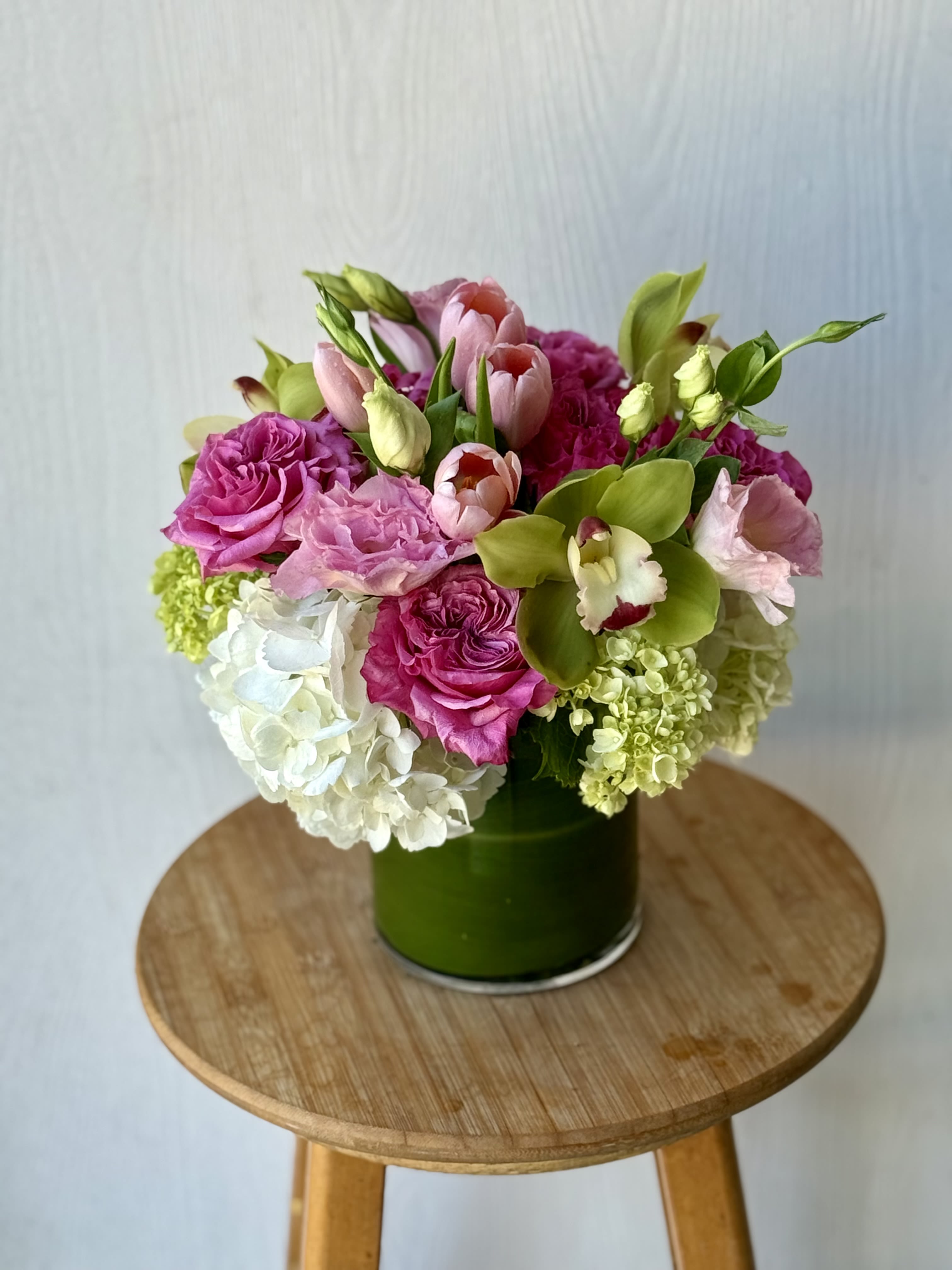 EC27 - Simple Beauty  - The Simple Beauty flower arrangement is the perfect combination of romance and sophistication and includes soft pink roses, white hydrangeas and delicate pink tulips. These fresh blooms are gorgeously arranged with vibrant green button mums which add texture and depth to the bouquet in a modern glass vase wrapped with a bright green leaf. This one-of-a-kind floral arrangement is a perfect choice for any special occasion, including weddings, birthdays, baby showers or even just an elegant and beautiful housewarming gift. 