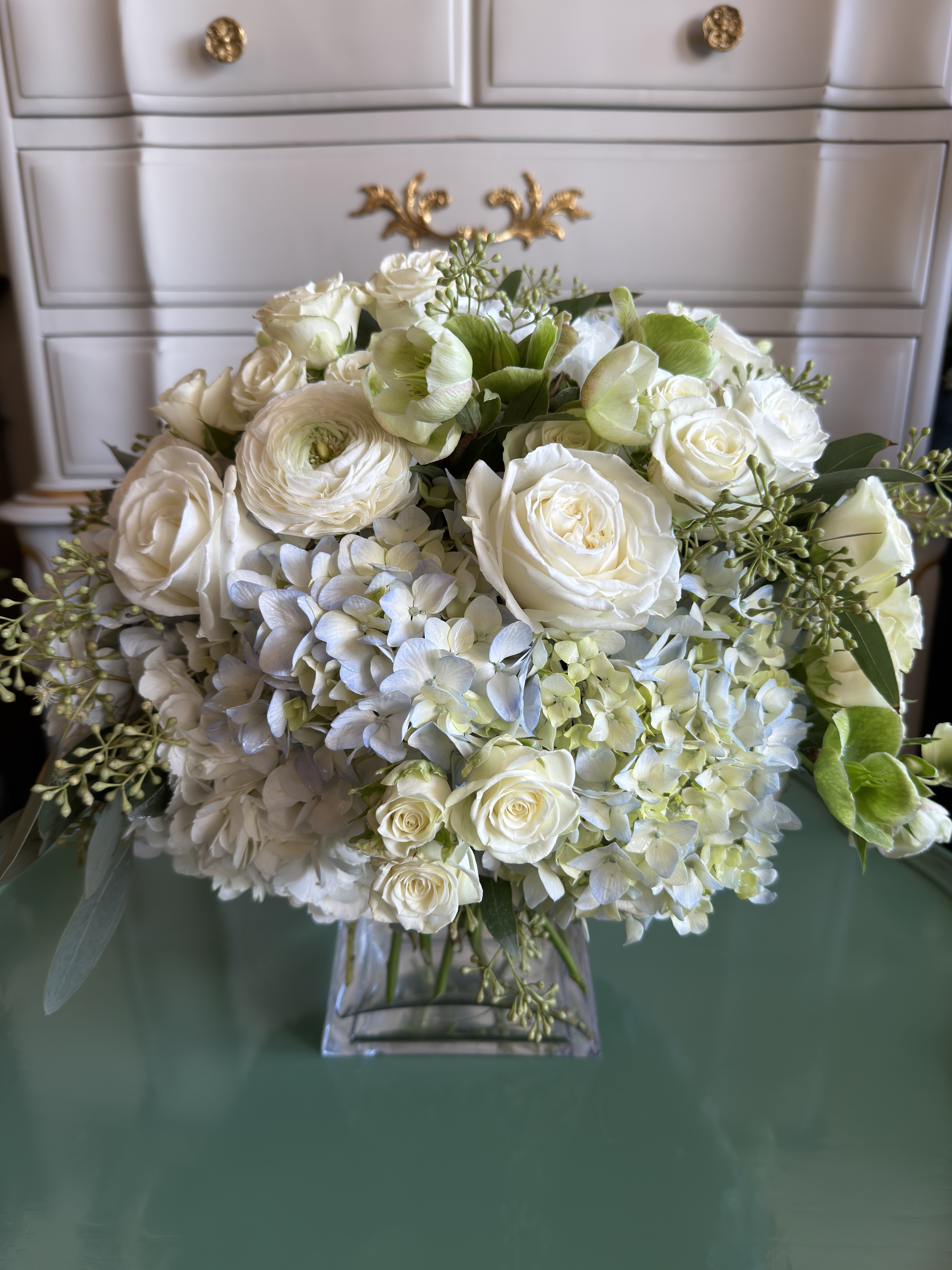 Lush and Layered Blues  - An elegant clear glass vase brimming with periwinkle blue hydrangea, white roses, white spray roses, and fresh eucalyptus. Lush, layered, and effortlessly chic—this piece is perfect for a holiday table, a welcoming entry, or as a thoughtful gift for your favorite hostess.  Please note: Seasonal flowers may vary based on availability, ensuring each arrangement is unique and fresh.  Freshness Guarantee: We stand behind our quality. Your flowers are guaranteed to look fresh and beautiful for 3–5 days from delivery.  To help them last:  •Top off the vase with clean water daily.  •Keep arrangements away from direct sun, heat, and drafts.  •Trim stems slightly after a couple of days if possible.