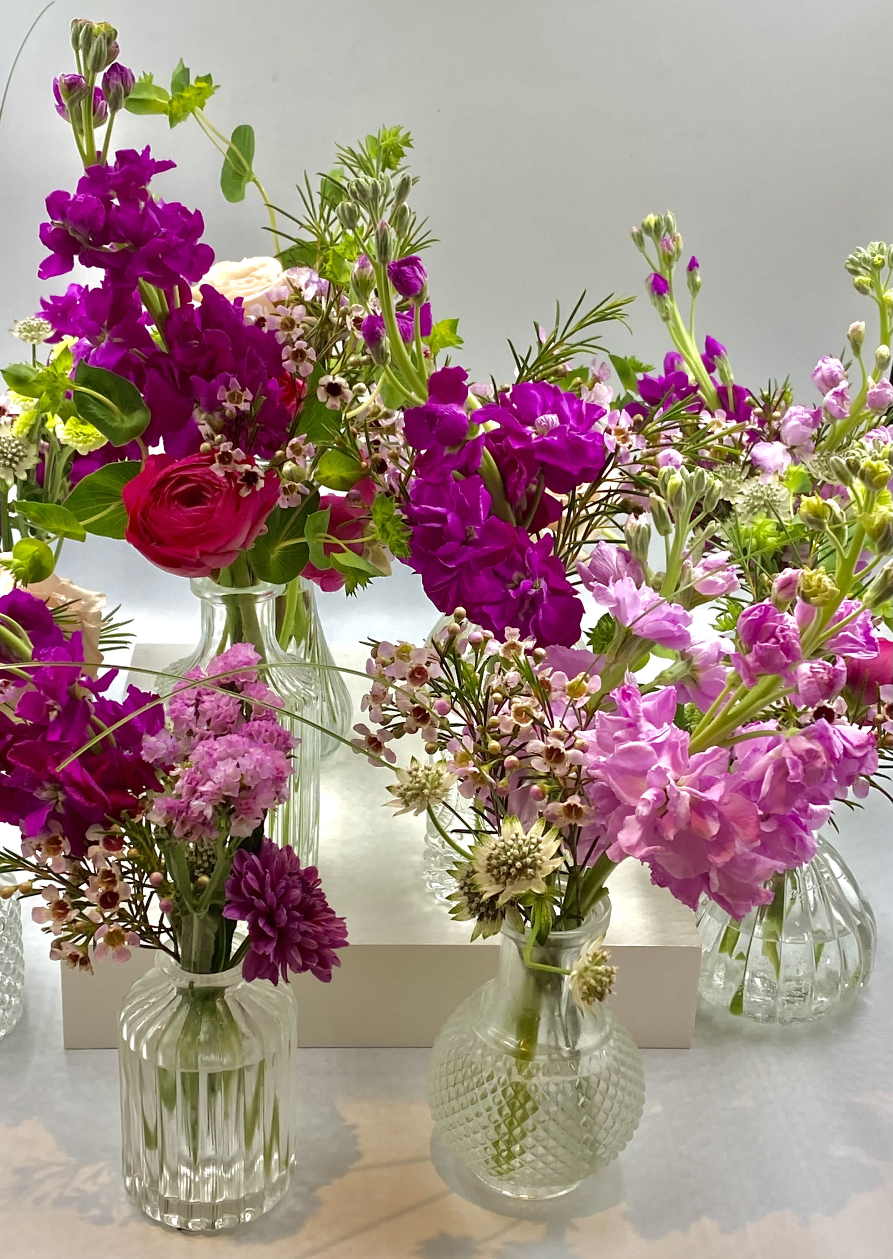 Assorted pink and purple flower arrangements in small glass vases