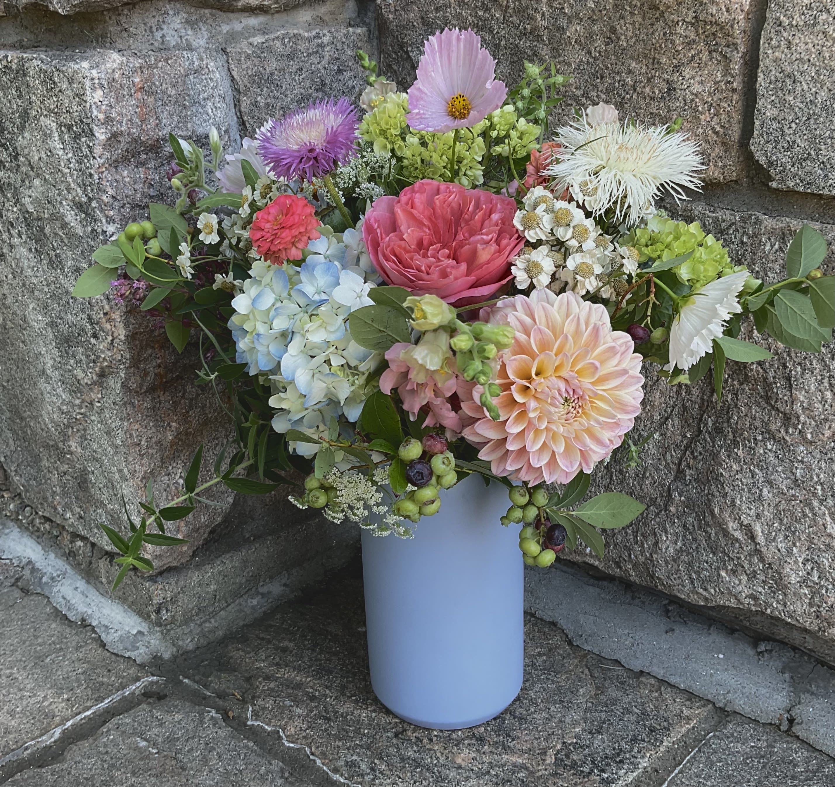 Mixed bouquet in a light blue vase with pink, peach, blue, and white blooms