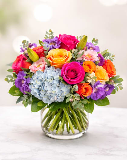 Colorful bouquet of roses, hydrangea, and lilies in a glass vase