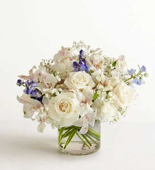 White rose bouquet with purple and pale blue flowers in a clear glass vase