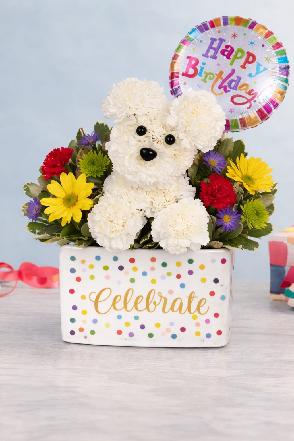 Birthday flower arrangement with white carnation dog, colorful blooms, and Happy Birthday balloon in a polka dot container