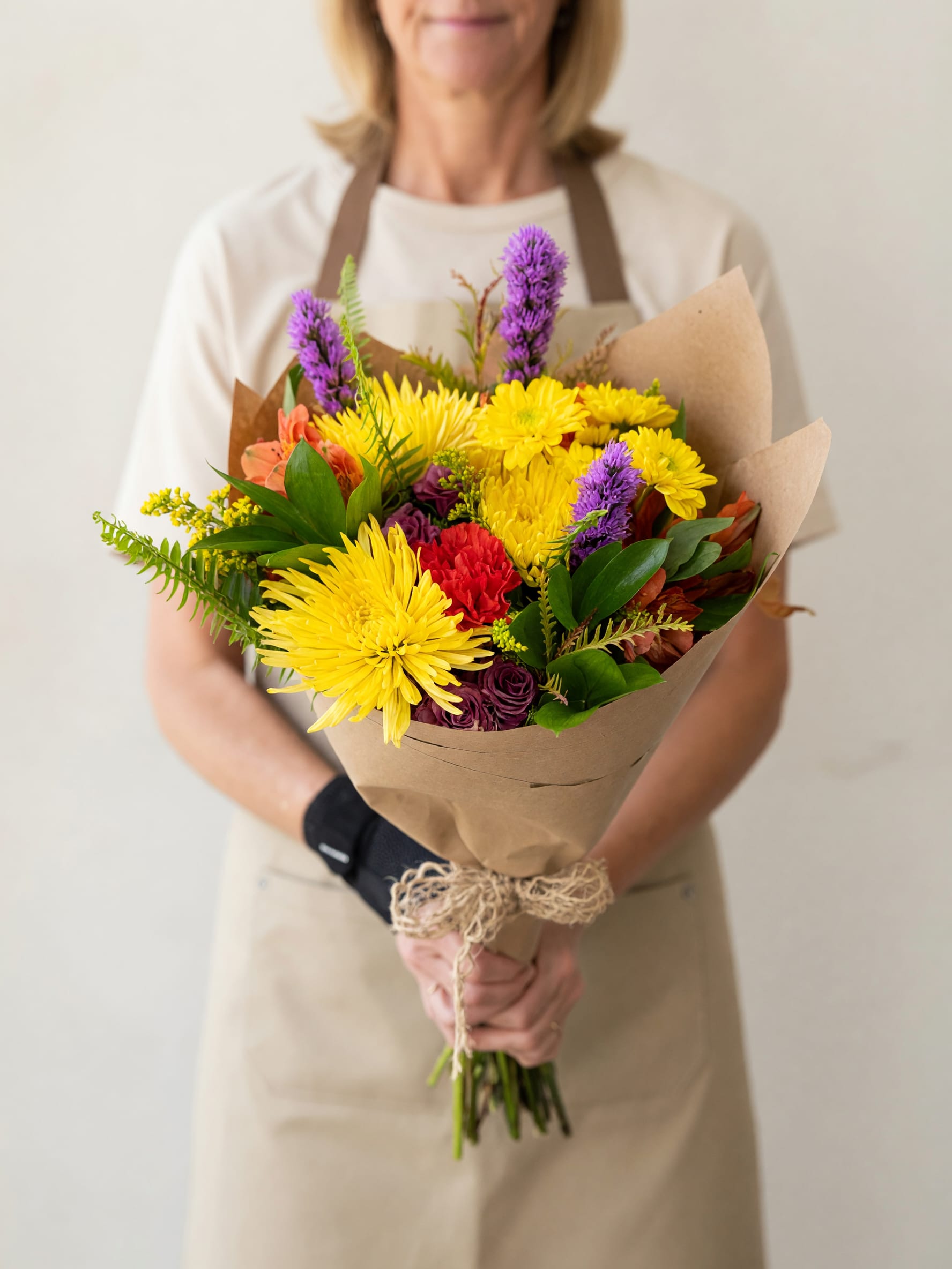 Person holding a colorful bouquet of yellow, purple, and red flowers wrapped in brown paper