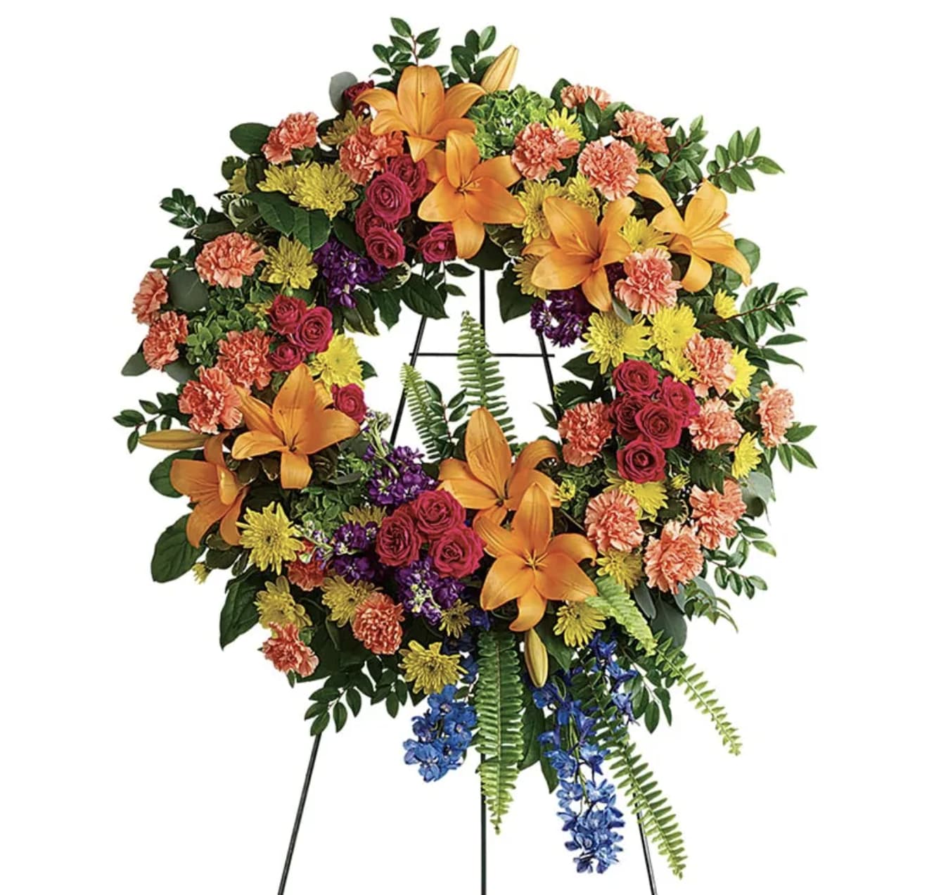 Colorful funeral wreath with lilies, roses, carnations, and blue accents on a stand