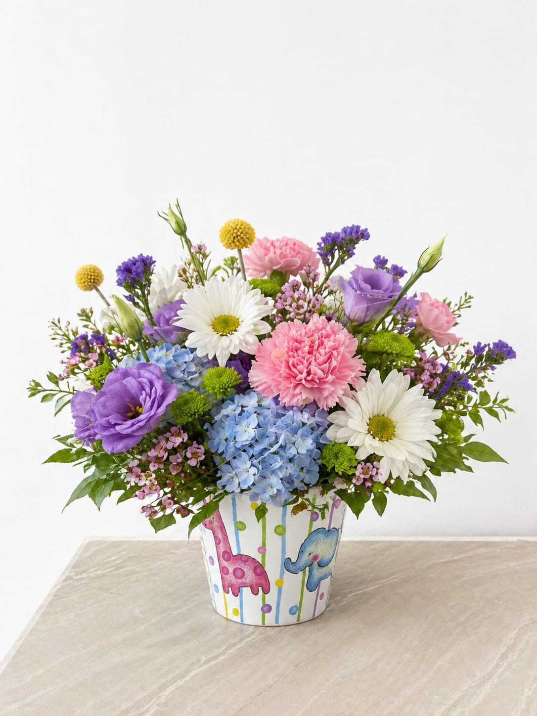 Sweet Safari Floral Arrangement - Whimsical, colorful, and full of charm, this cheerful arrangement is designed in an adorable keepsake container featuring playful safari animals. A vibrant mix of soft blue hydrangea, pink carnations, lavender blooms, and crisp white daisies is accented with pops of yellow and fresh greenery, creating a fun and lively garden-inspired design.  The combination of pastel tones and bright accents makes this arrangement perfect for baby showers, birthdays, or welcoming a new little one. Its joyful, lighthearted style adds a sweet touch to any space while the reusable container makes it a lasting keepsake.  Each arrangement is handcrafted with care, ensuring a full, balanced look that highlights every beautiful bloom.