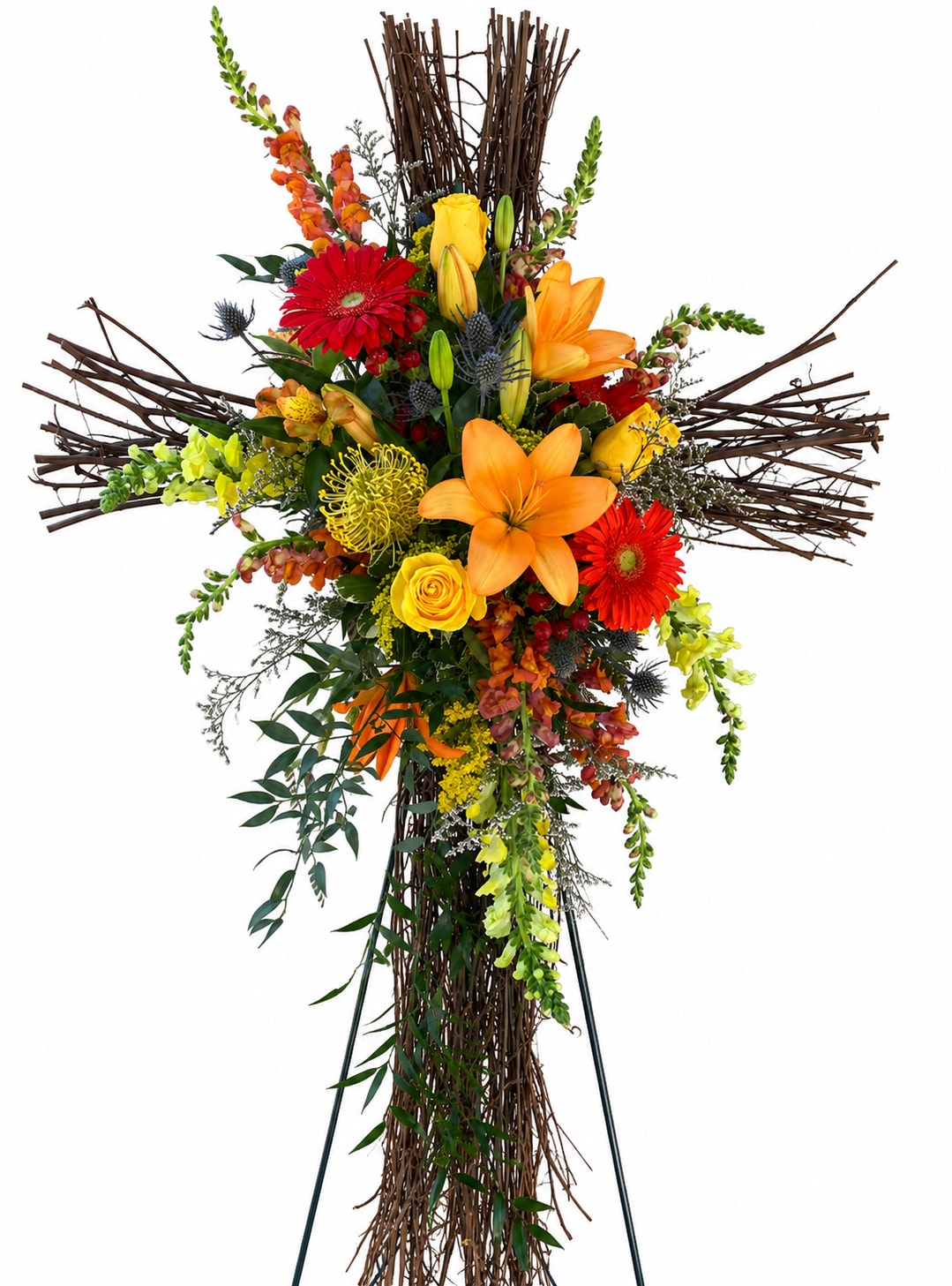 Forever Grapevine Cross - A bright, devotional cross crafted on a tall twig framework, this funeral flower arrangement pairs vivid orange lilies, yellow roses and red gerbera daisies with snapdragons and smaller accent blooms to create a warm, uplifting memorial display. The cross shape and rustic brown branches give it a formal, reverent presence ideal for sympathy services or to mark a meaningful remembrance, while the saturated palette brings an optimistic, life-affirming energy to the tribute.  Designed to stand upright on a sturdy metal easel, the piece is densely layered for strong visual impact from the front and at service viewings. Orange lilies add height and fragrance, yellow roses provide sunny focal points, red gerberas contribute bold color contrast, and snapdragons plus delicate fillers fill in texture and movement. The twig cross stand remains visible around the blooms, offering a handcrafted, natural contrast to the saturated flowers and deep green foliage.  Made for honoring someone special, this arrangement reads as both devotional and celebratory-the kind of tribute that lets the person you're remembering feel seen and remembered. Size and exact flower counts are built to create a full, standing cross appropriate for funerals and memorial services; please contact us if you need specific dimensions or customization for service placement.