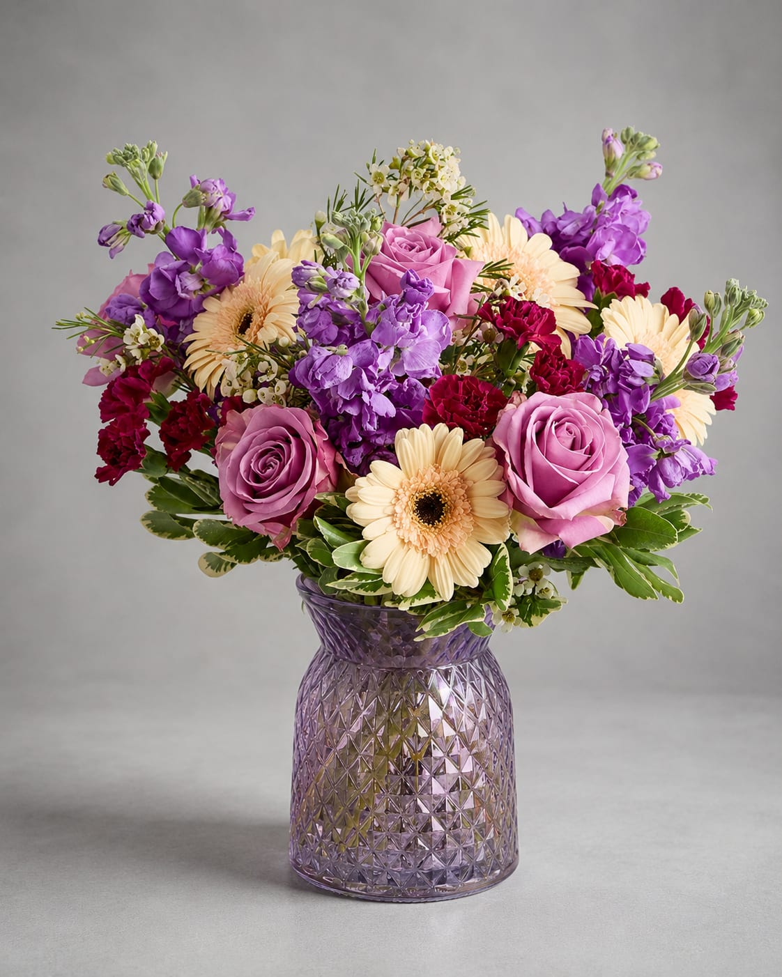 Purple and pink bouquet with cream daisies in a textured glass vase