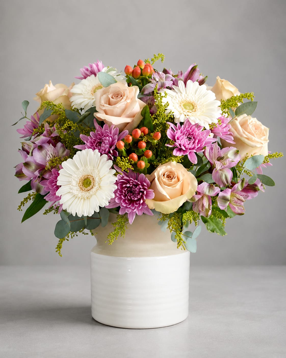 Mixed bouquet of roses, gerbera daisies, and purple blooms in a white vase