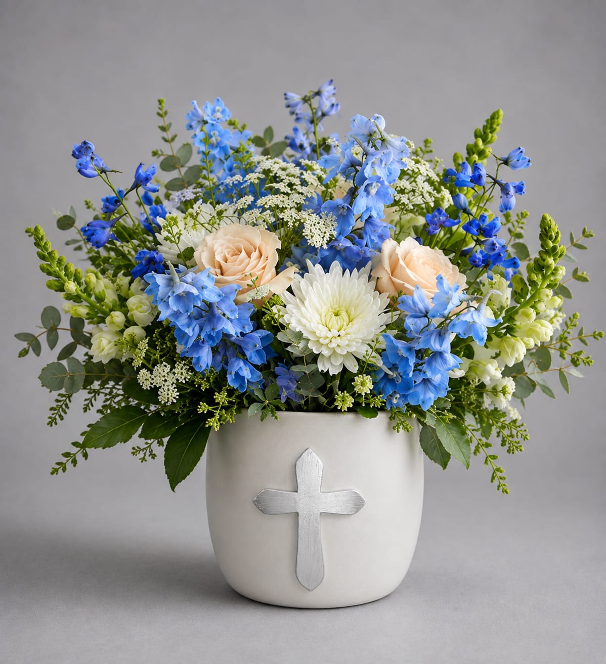 Blue and white floral arrangement in a white vase with a cross emblem