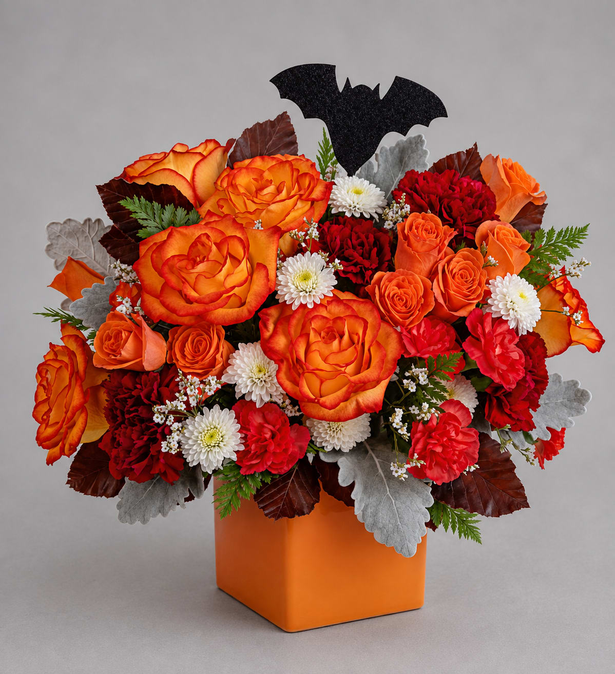 Orange and red rose arrangement in an orange vase with a bat pick
