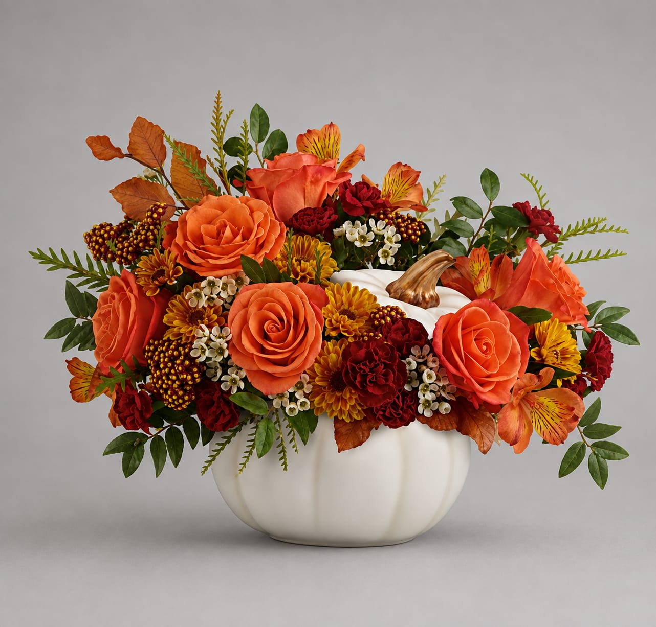 Orange and red floral arrangement in a white pumpkin vase