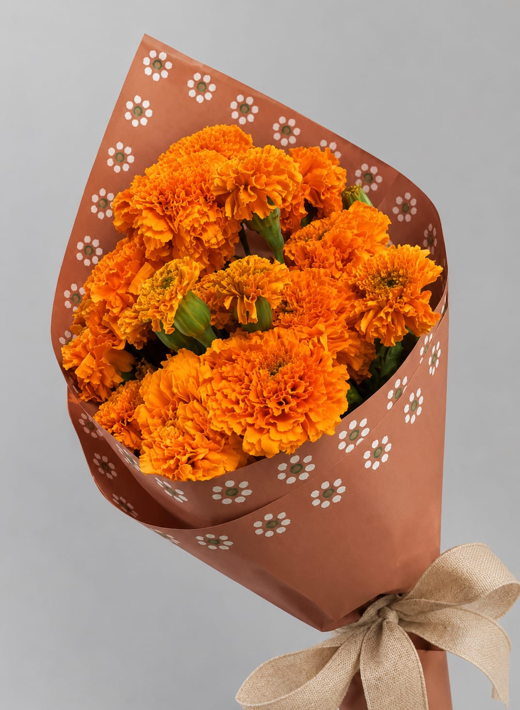 Bouquet of orange marigolds wrapped in patterned brown paper with a burlap bow