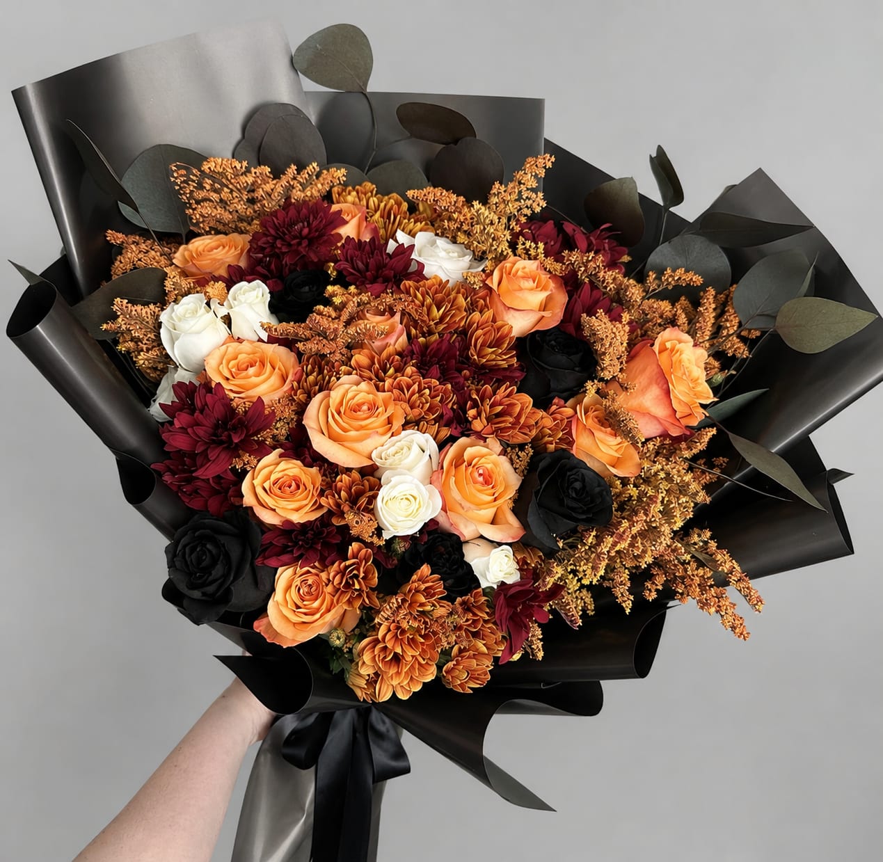 Bouquet of orange, white, and dark red flowers wrapped in black paper