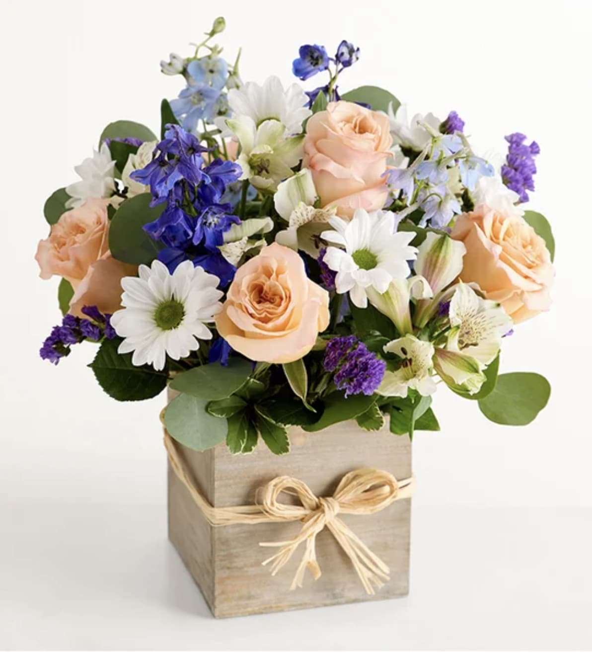 Bouquet of peach roses, white daisies, and blue flowers in a wooden box