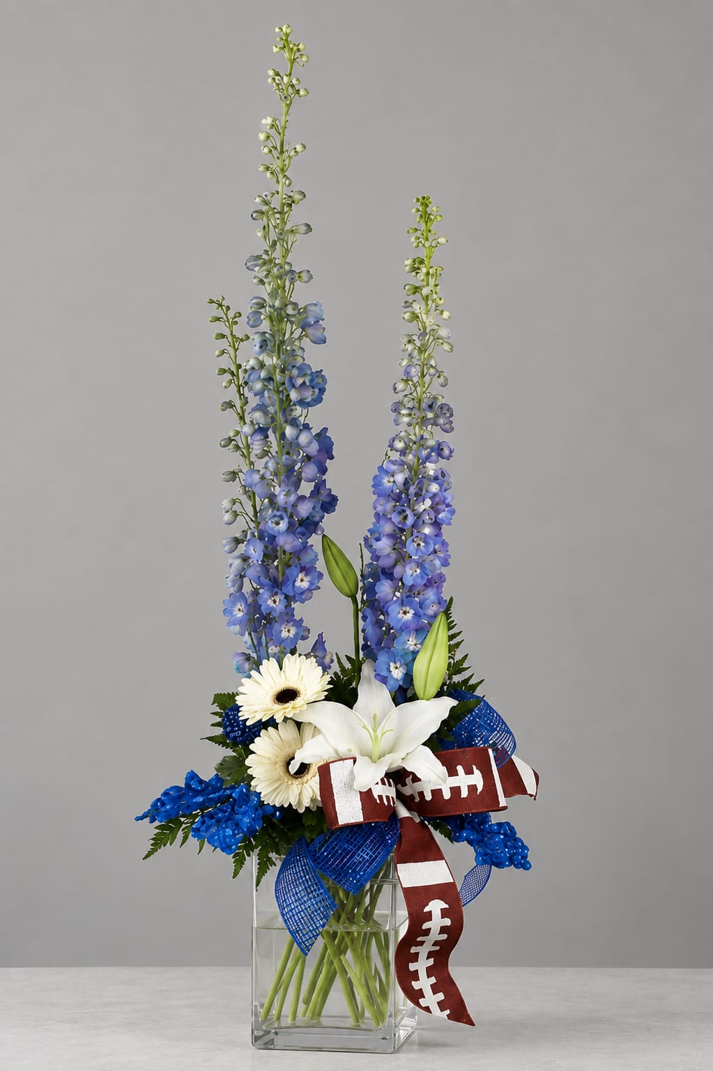 Tall blue and white floral arrangement in a clear glass vase with football ribbon