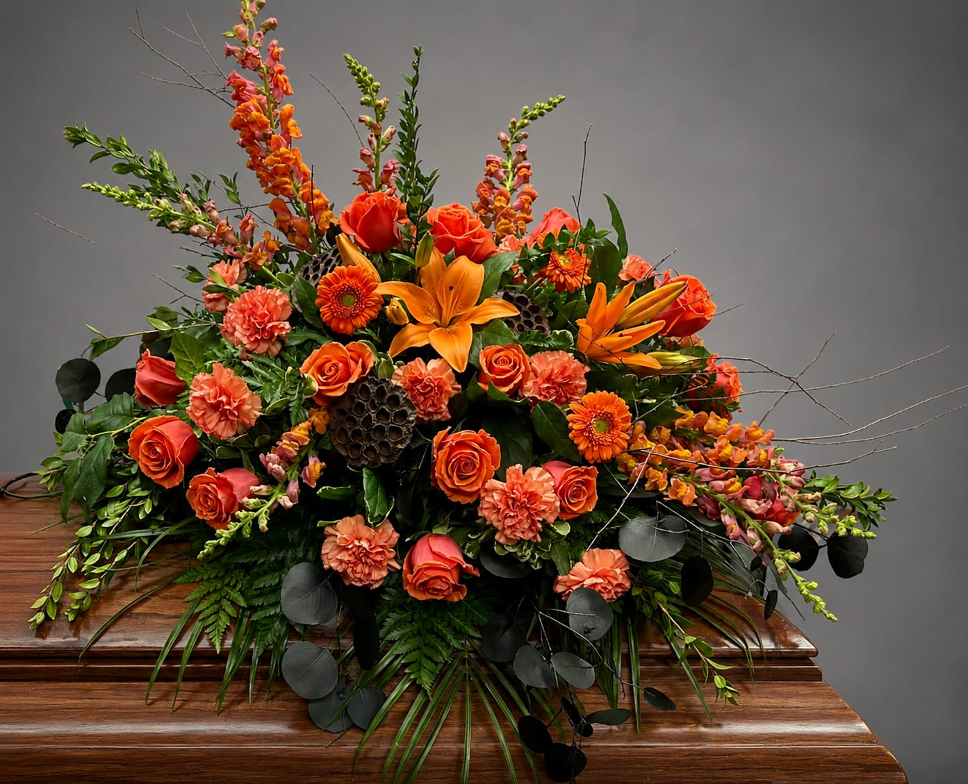 Orange floral casket spray with roses, lilies, and carnations