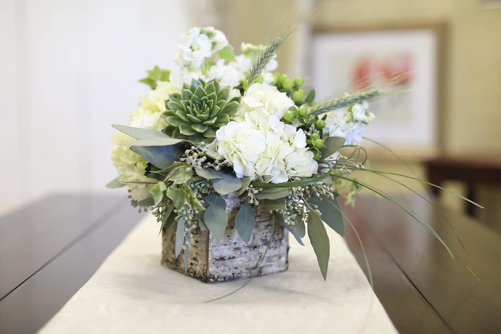 White floral arrangement in a birch bark container with green succulents