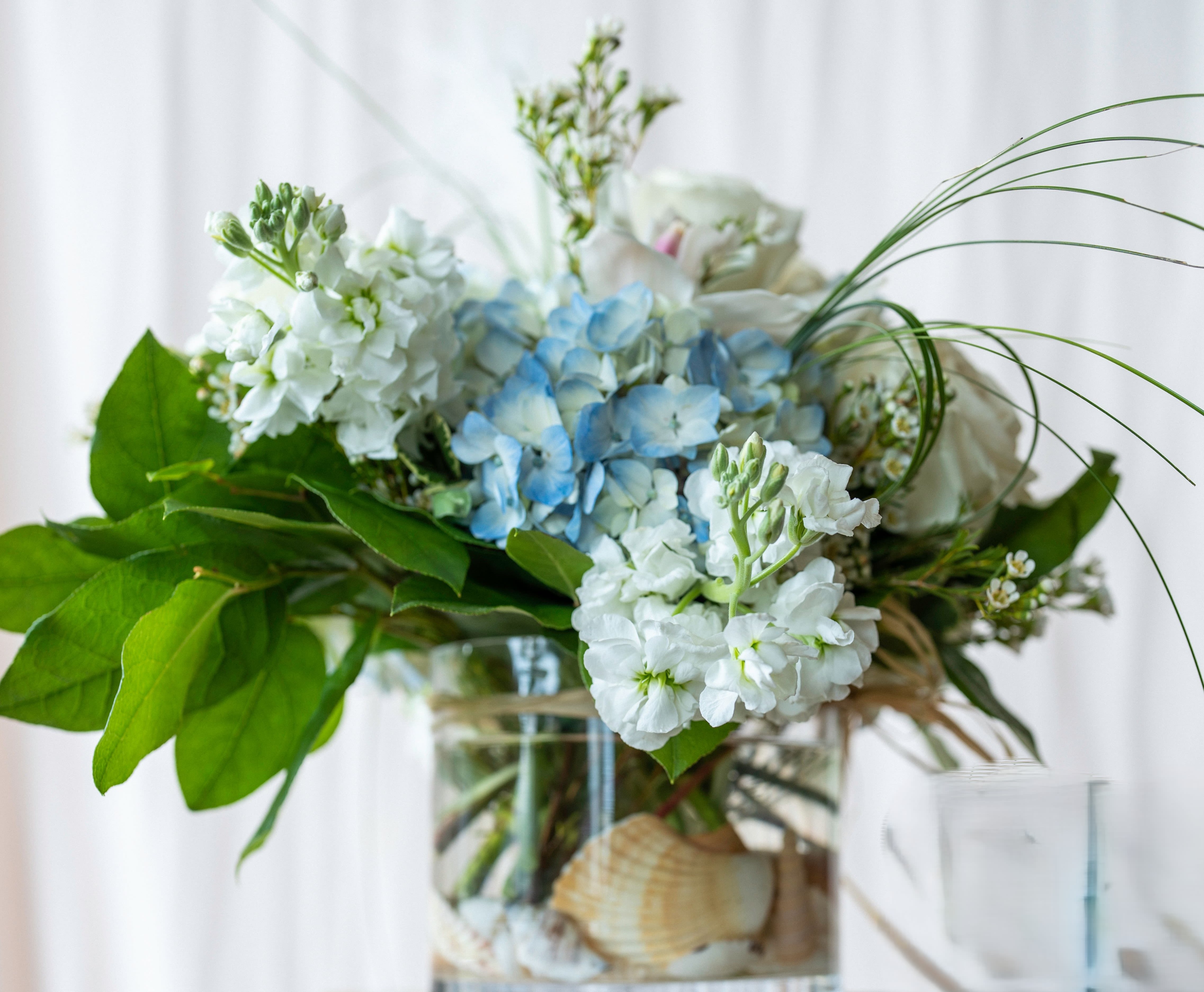 Blue and white flowers arranged in a glass vase with broad green leaves
