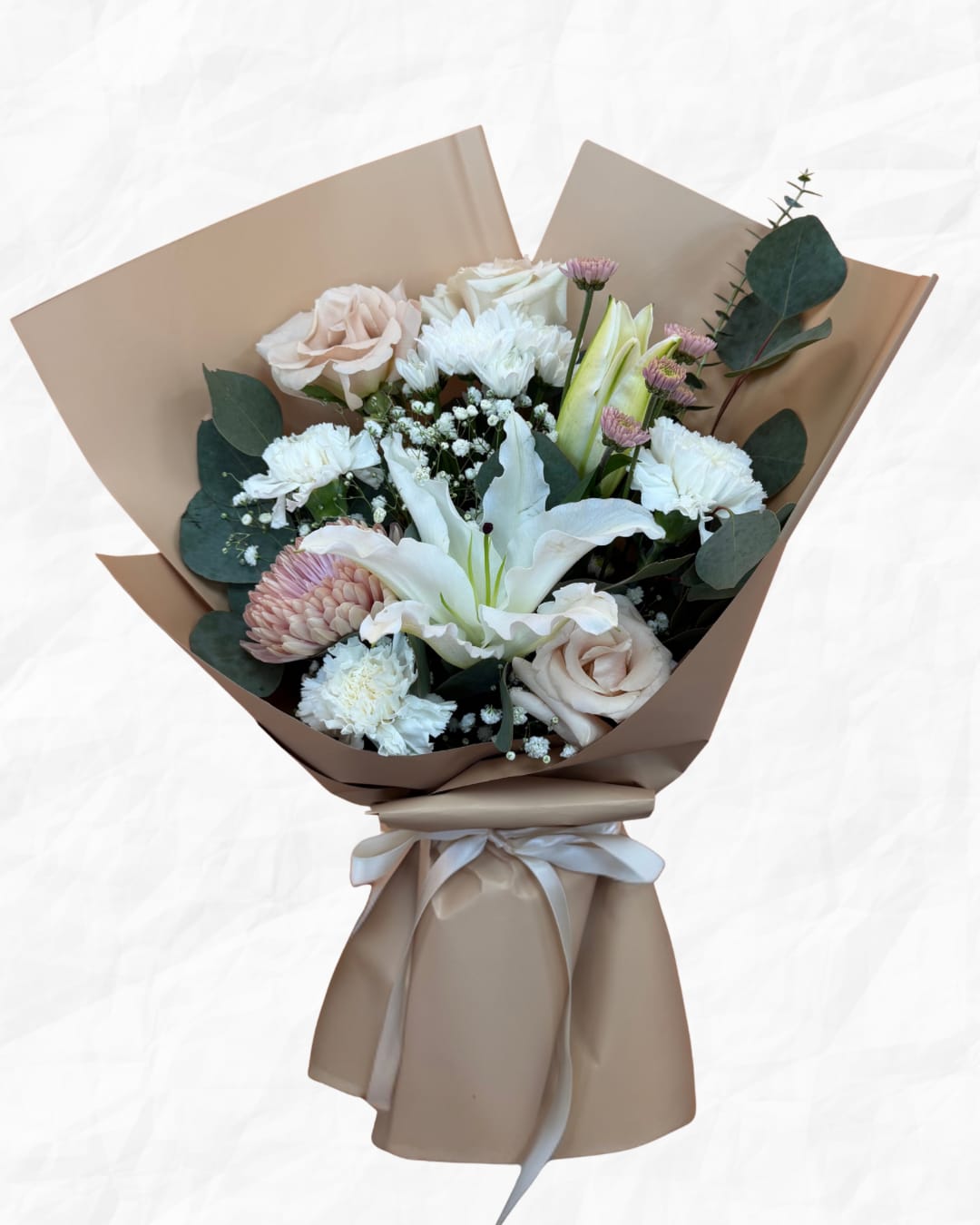 Bouquet of pale roses, white lilies, and chrysanthemums wrapped in tan paper