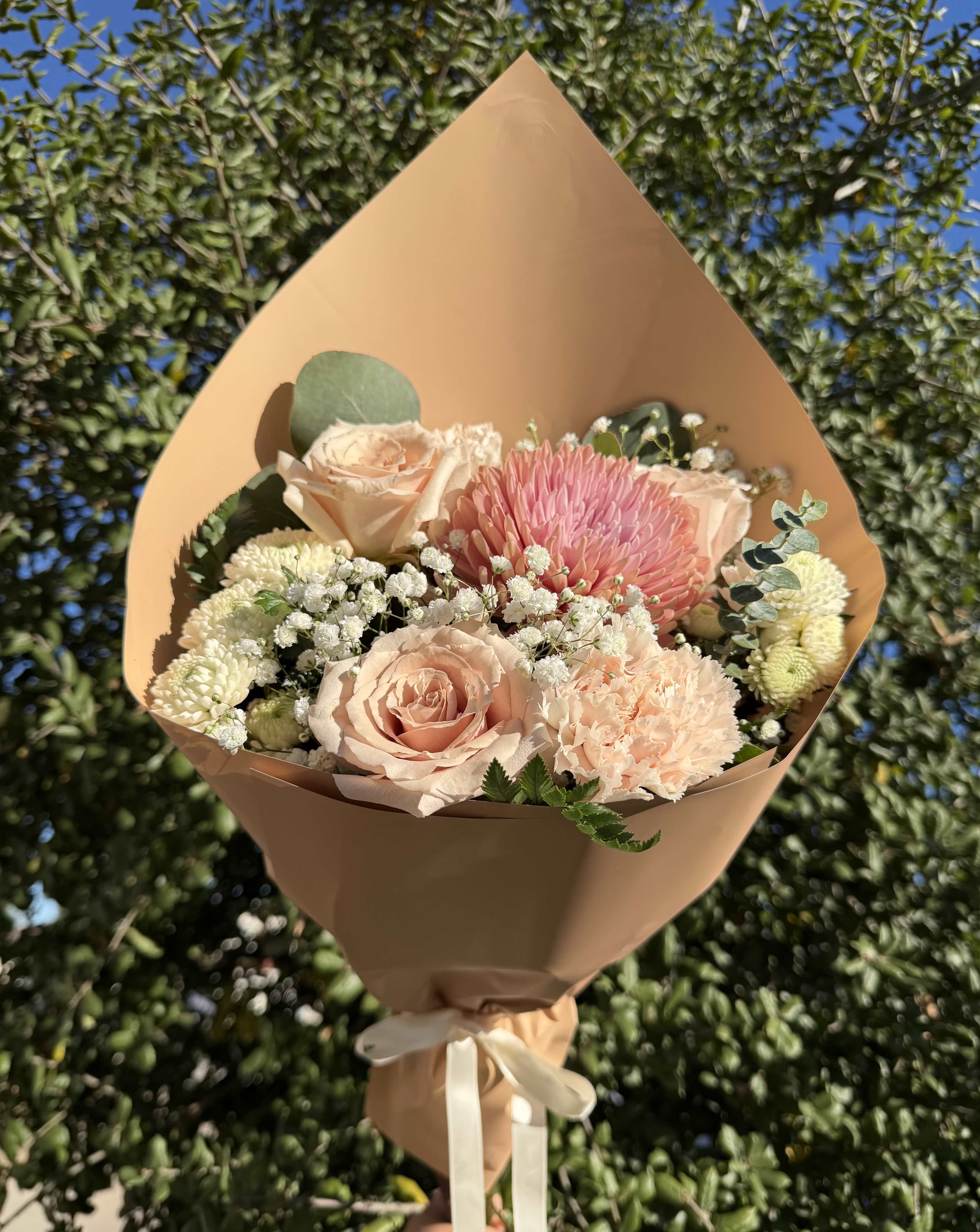 Bouquet of blush roses, pink chrysanthemum, and white filler flowers in tan wrap