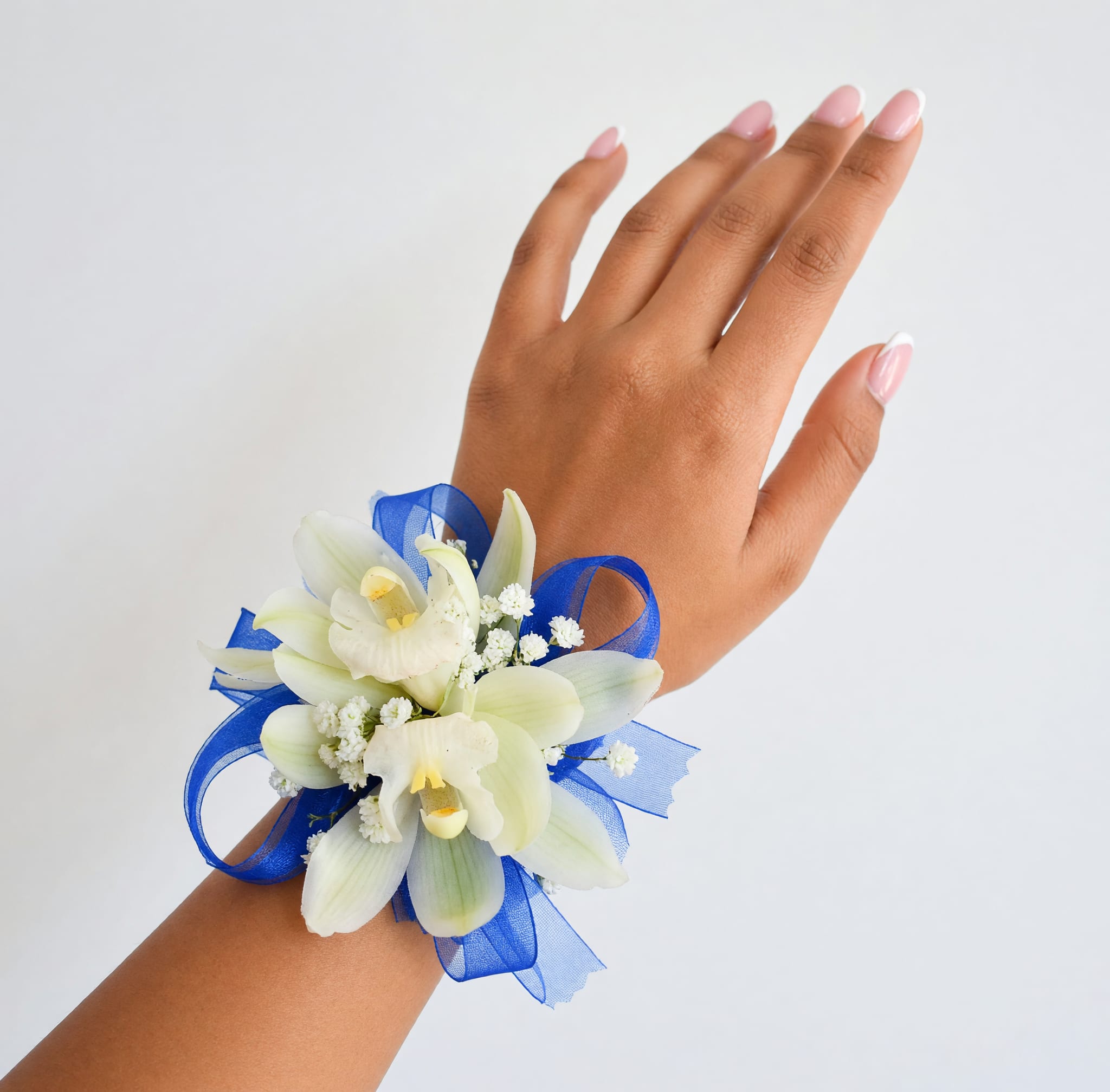 White orchid wrist corsage with blue ribbon on a hand