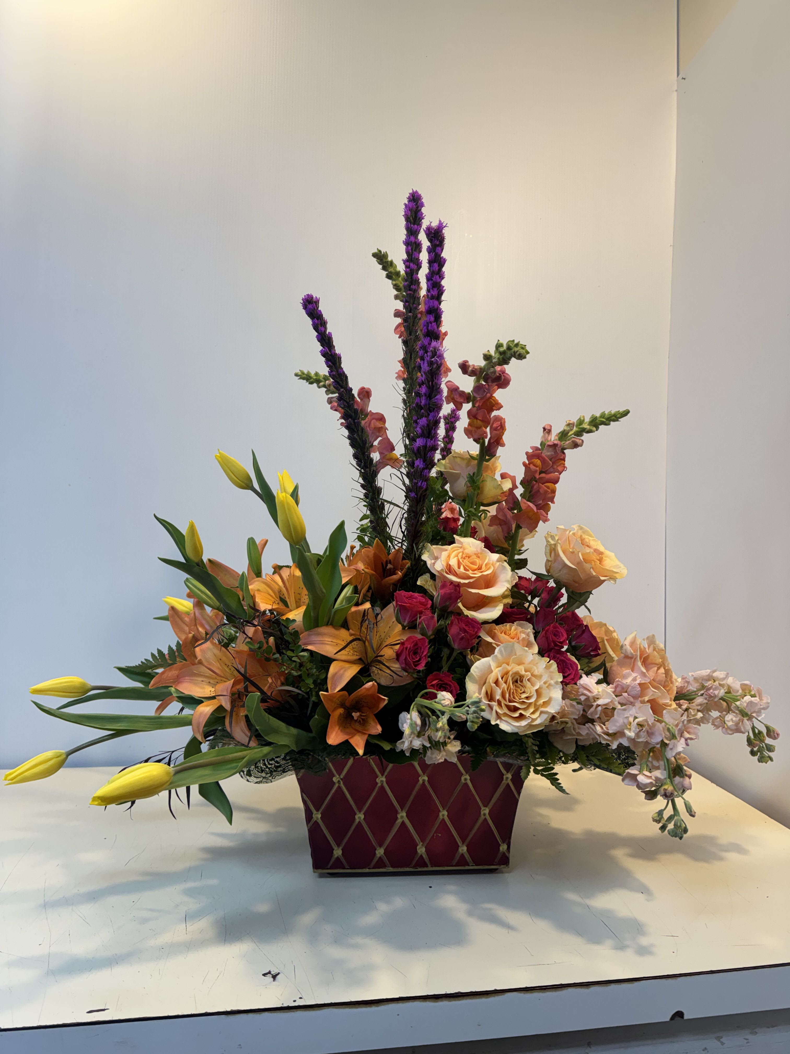 Mixed bouquet in a burgundy rectangular container with roses and lilies