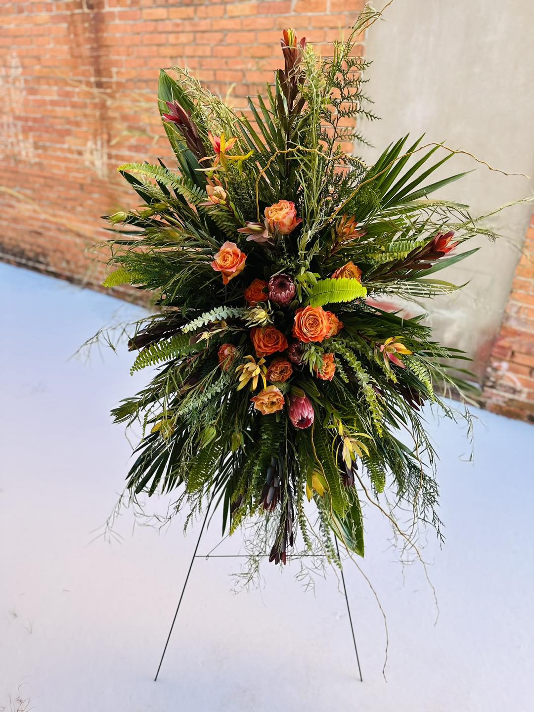 Tall tropical floral spray with orange roses and mixed greenery on a stand