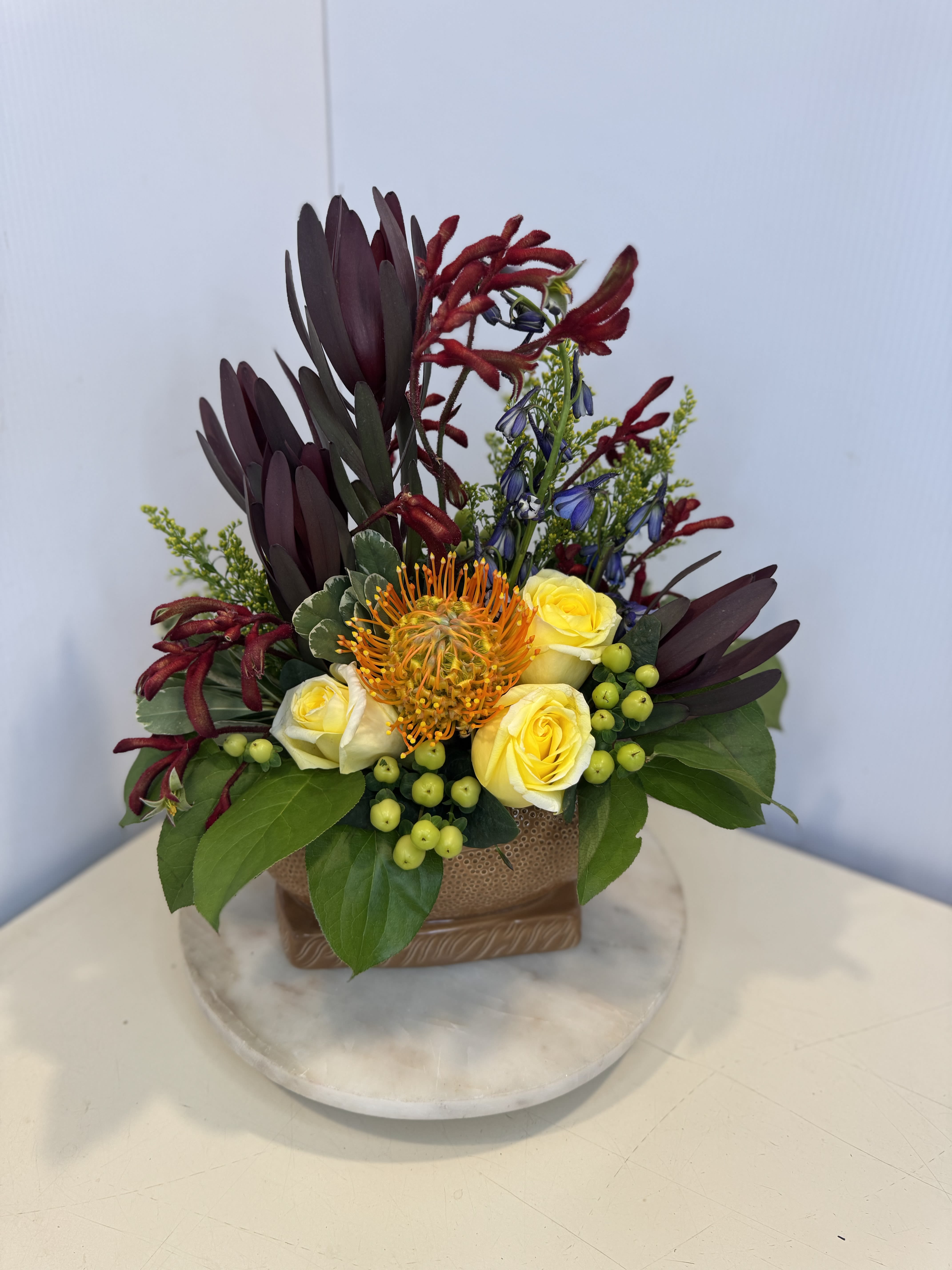 The MVP Arrangement - Touchdown-worthy and designed with Dad in mind! This bold arrangement features striking pincushion protea, premium roses, rich foliage, and unique textural blooms, all arranged in a football-themed container. Perfect for celebrating the coach, MVP, and biggest fan in your life this Father's Day!