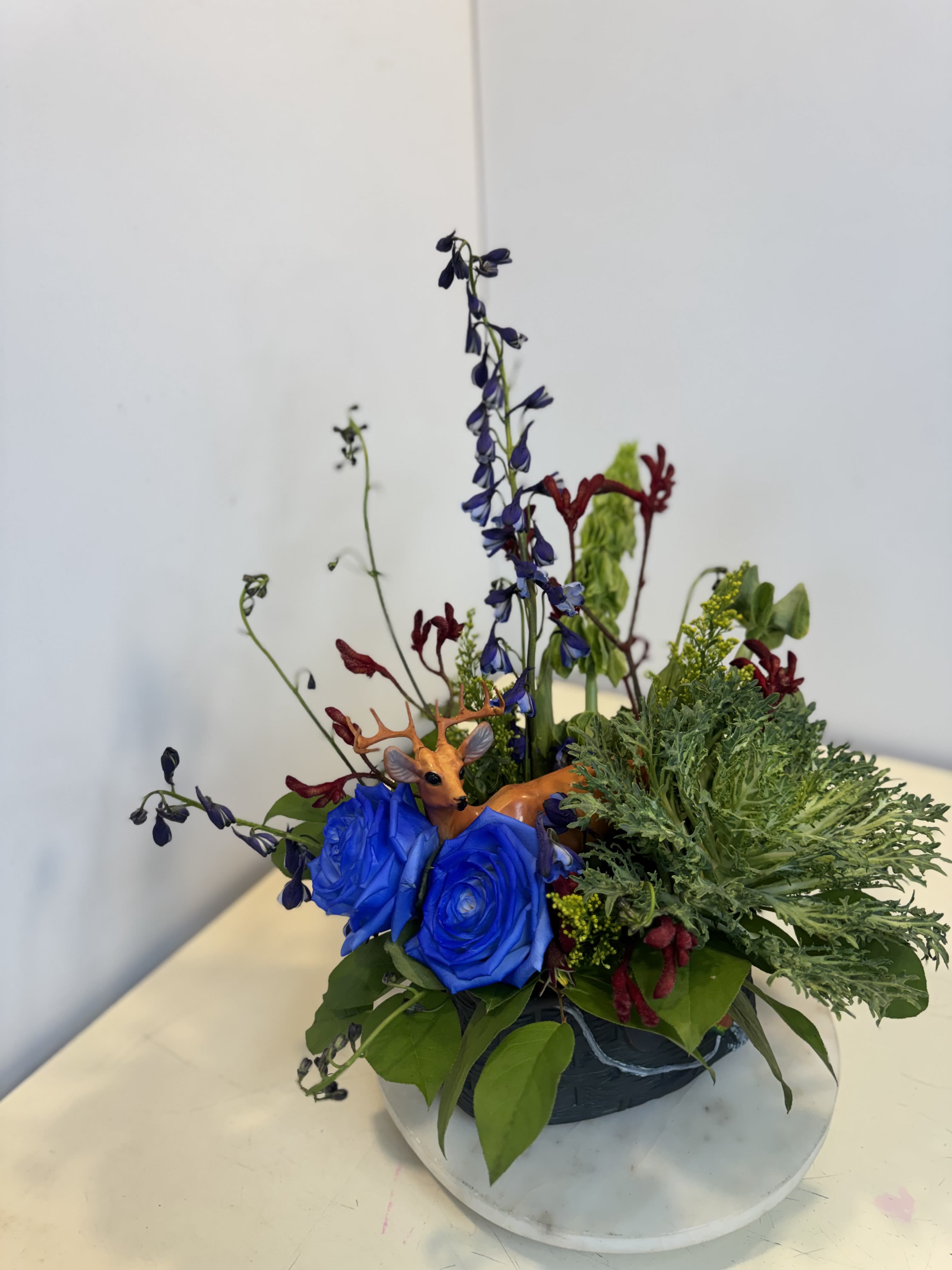 Deerly Loved Arrangement - Celebrate the outdoorsman in your life with this unique Father's Day design featuring vibrant blue roses, lush greenery, natural textures, and a charming deer accent. Inspired by the beauty of the great outdoors, this arrangement is perfect for dads who love hunting, nature, and spending time in the woods. A thoughtful gift that's ss one-of-kind as he is.