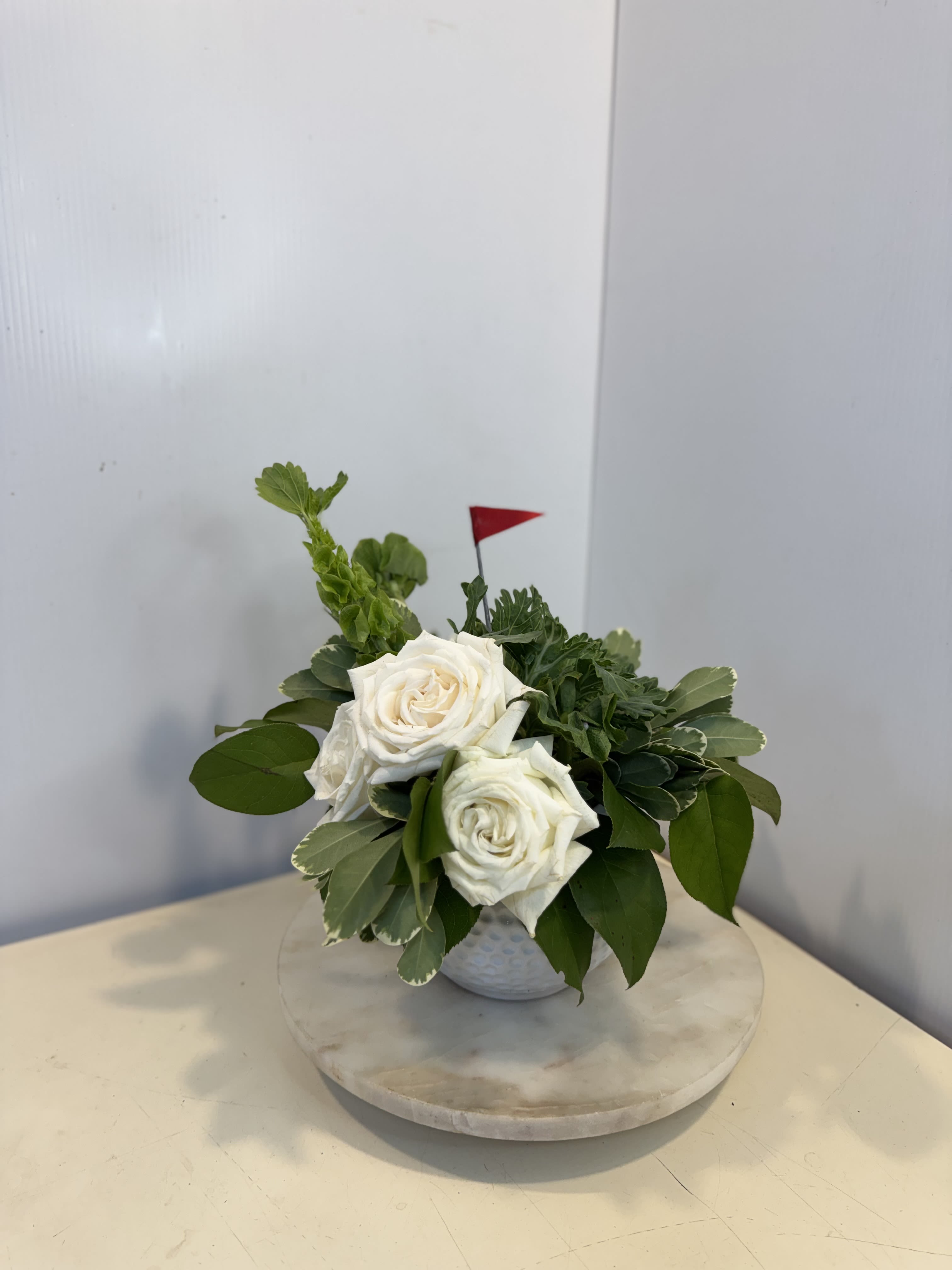 Dad's Hole-in-One - Celebrate Dad with a gift that's right on par! Designed in a charming golf ball ceramic container, this classic arrangement features elegant white roses, kale, fresh greenery, and natural textures for a clean, sophisticated look. Perfect for the golf-loving dad, grandpa, or favorite golfing partner, this thoughtful design is a winning way to show your appreciation this Father's Day.