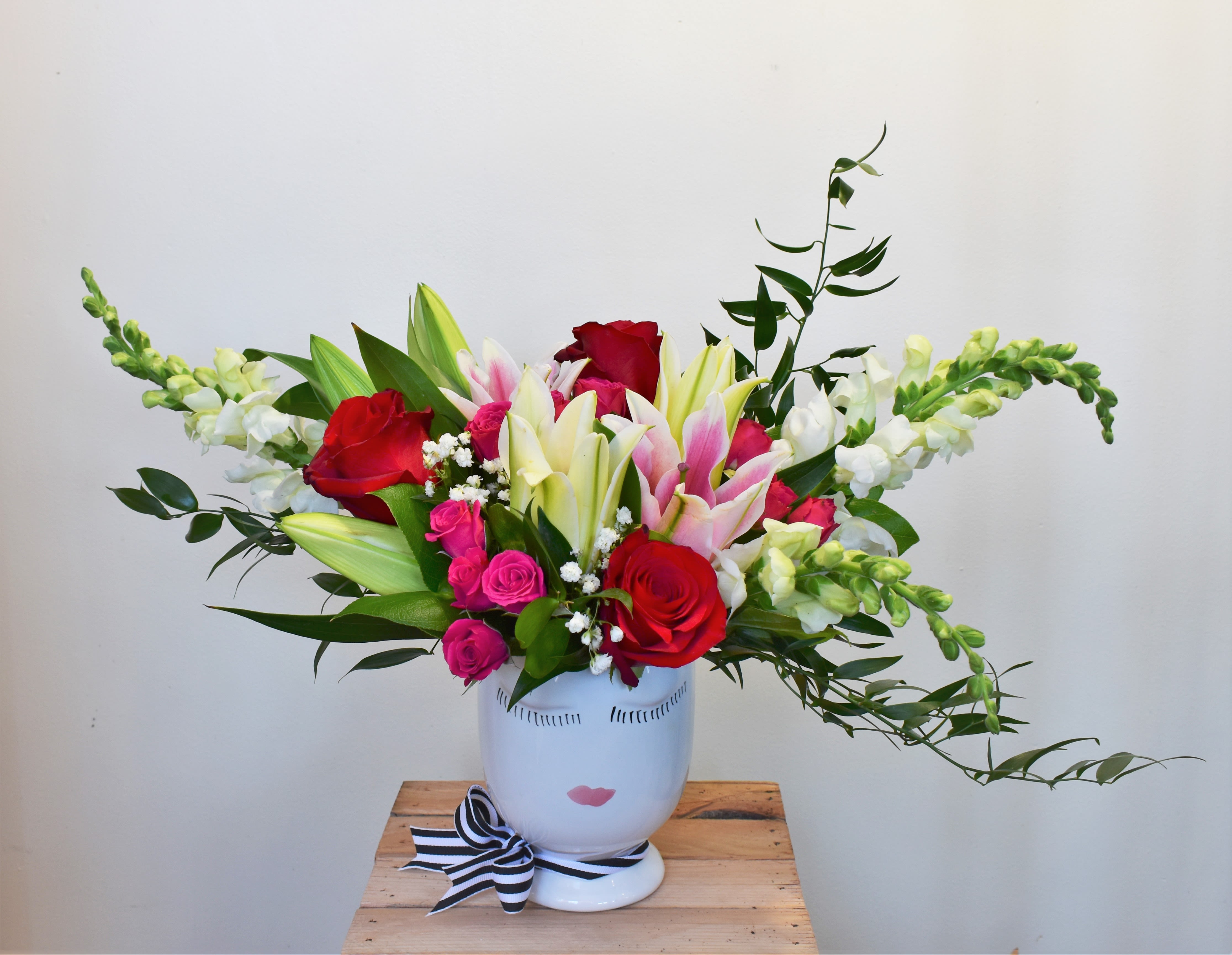Bouquet of red and pink roses with lilies in a white face vase