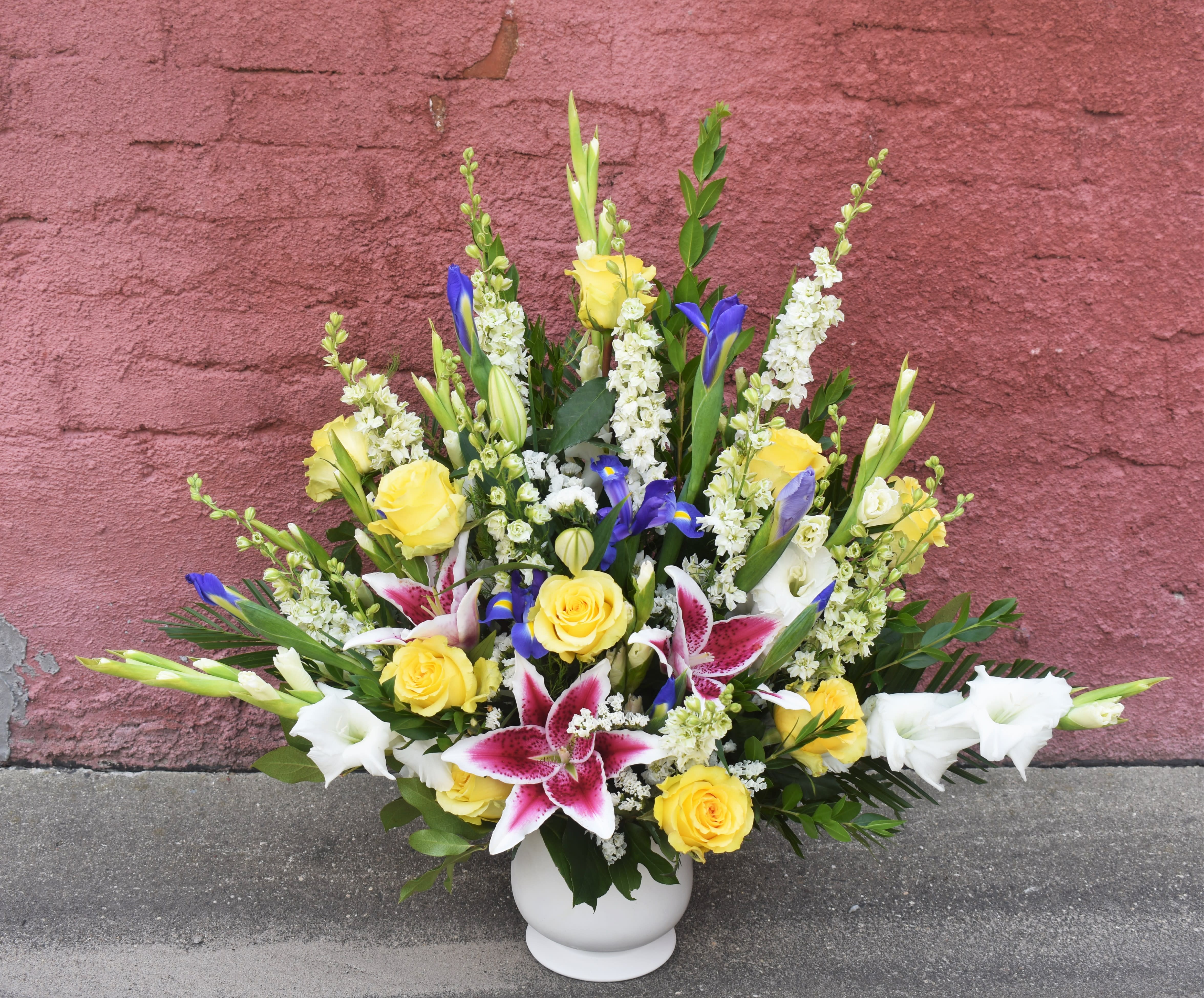 Mixed bouquet of yellow roses, white lilies, and blue irises in a white vase