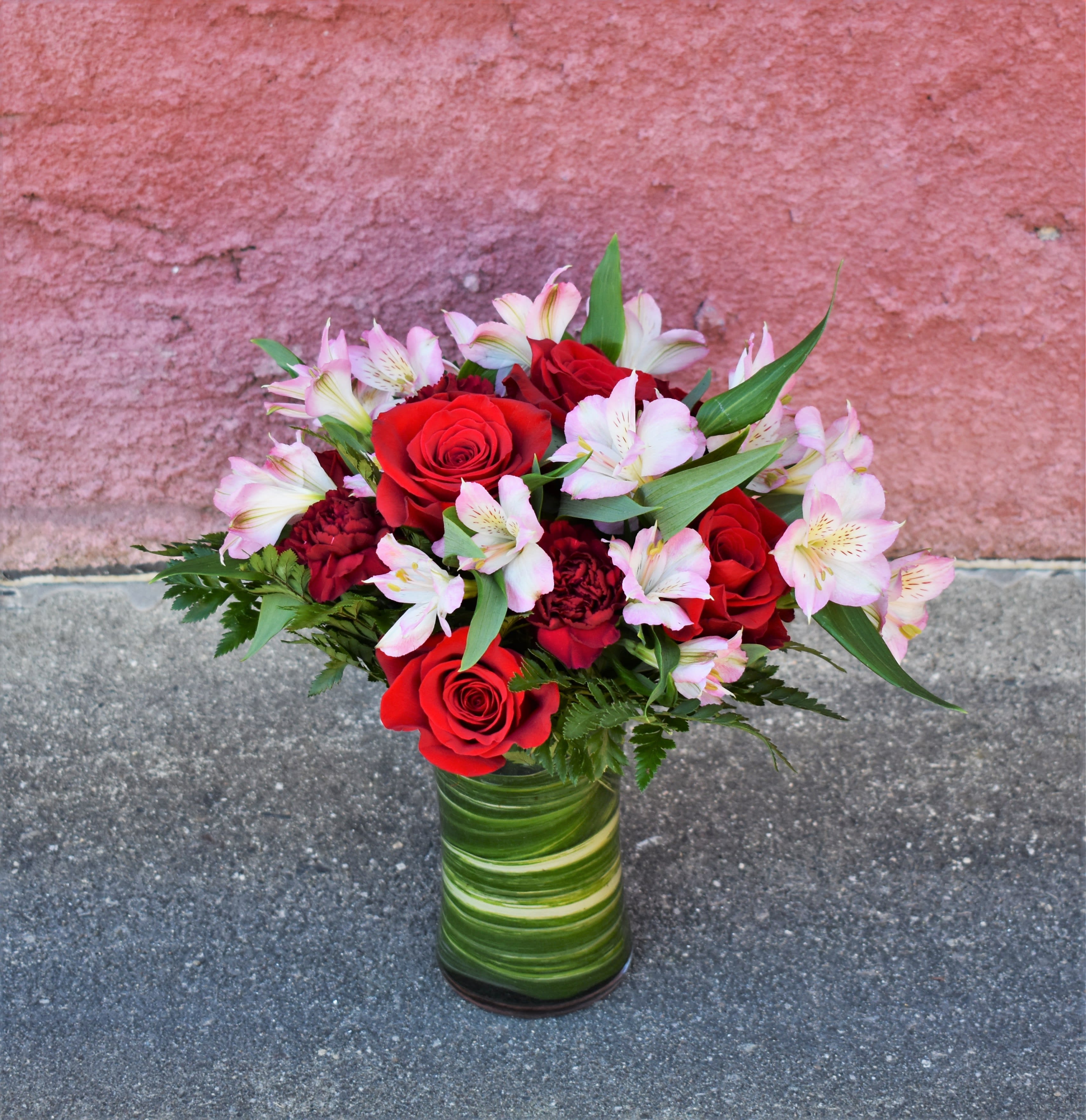 Blooming Love - This bouquetis the perfect expression of sweet affection and adoration. Rich red roses, burgundy carnations, pink Peruvian lilies, and lush greens are gorgeously arranged in a clear glass vase lined with a ti leaf to create a stunning way to convey your most heartfelt emotions.