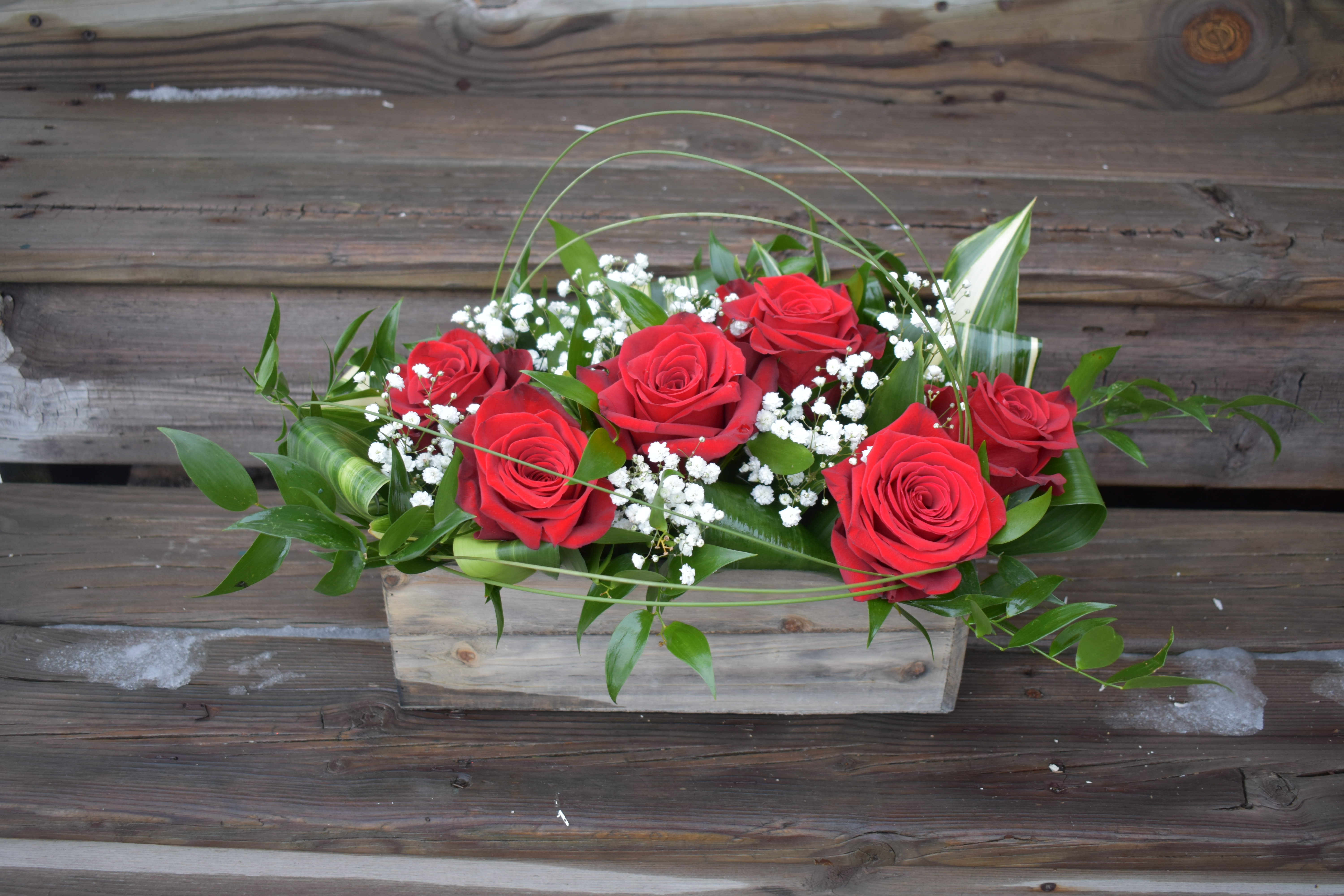 Red roses arranged in a rectangular wooden box with white filler flowers