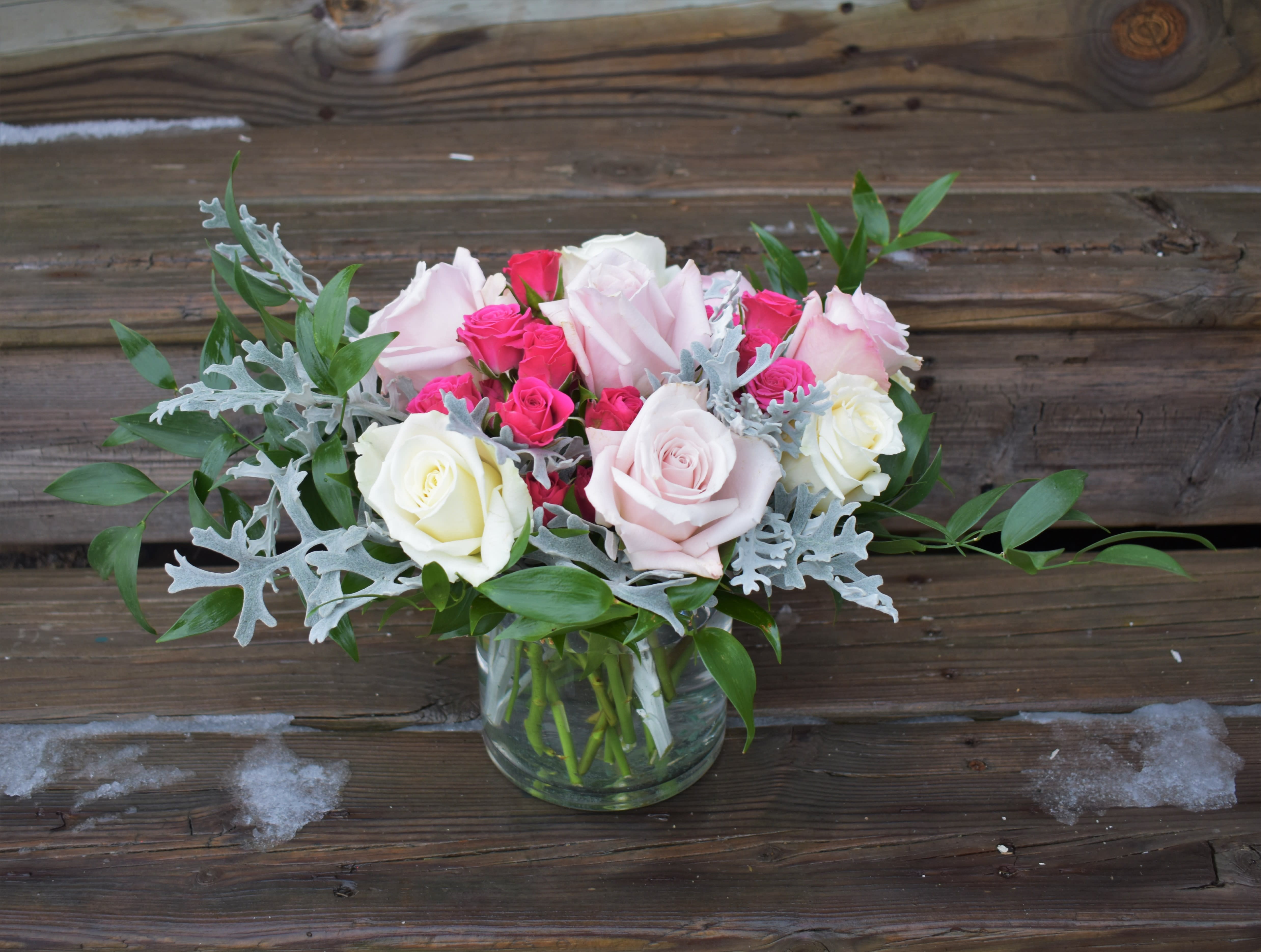 Pink and white roses in a glass vase with silver foliage