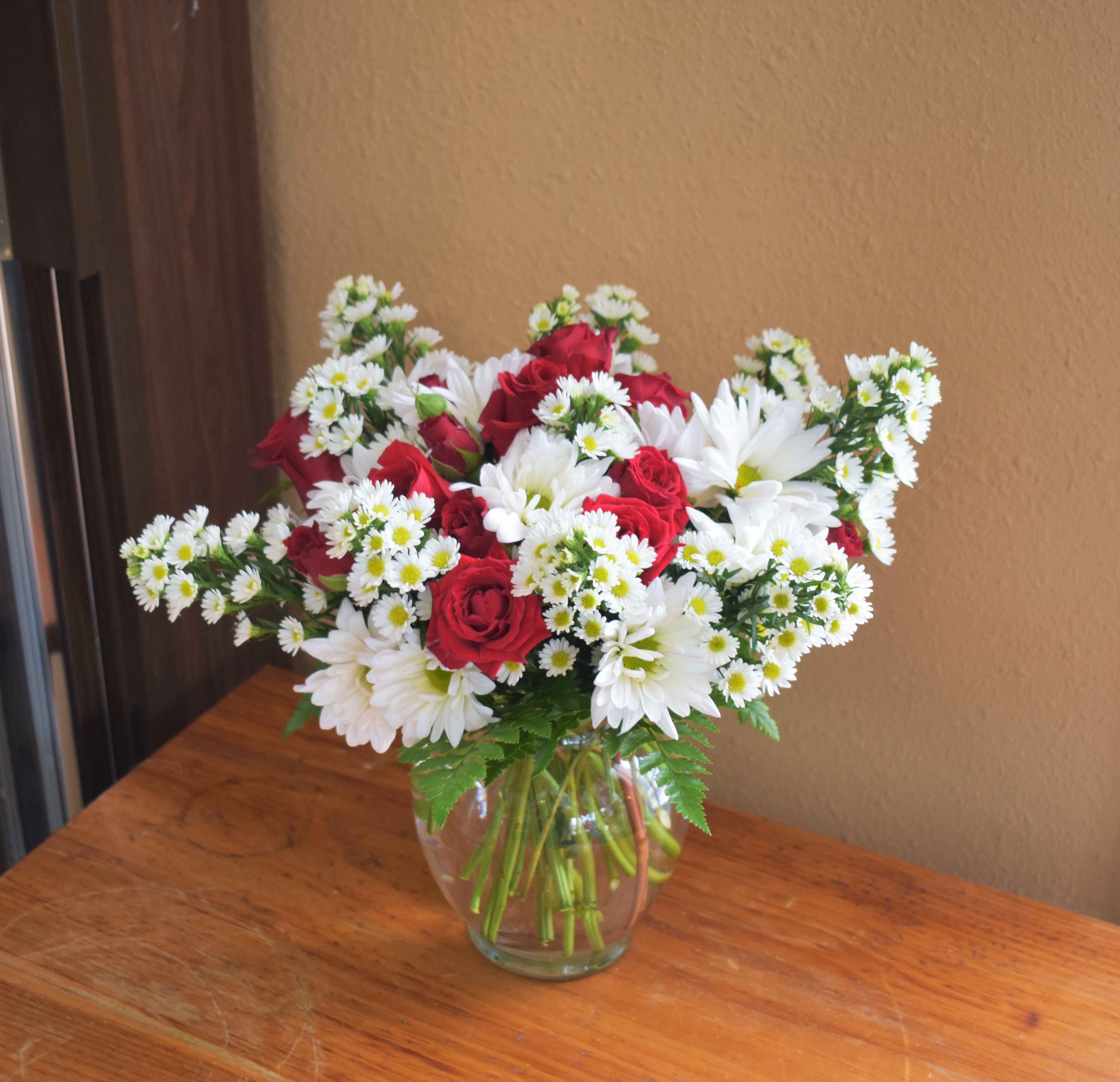 Red roses and white daisies arranged in a clear glass vase